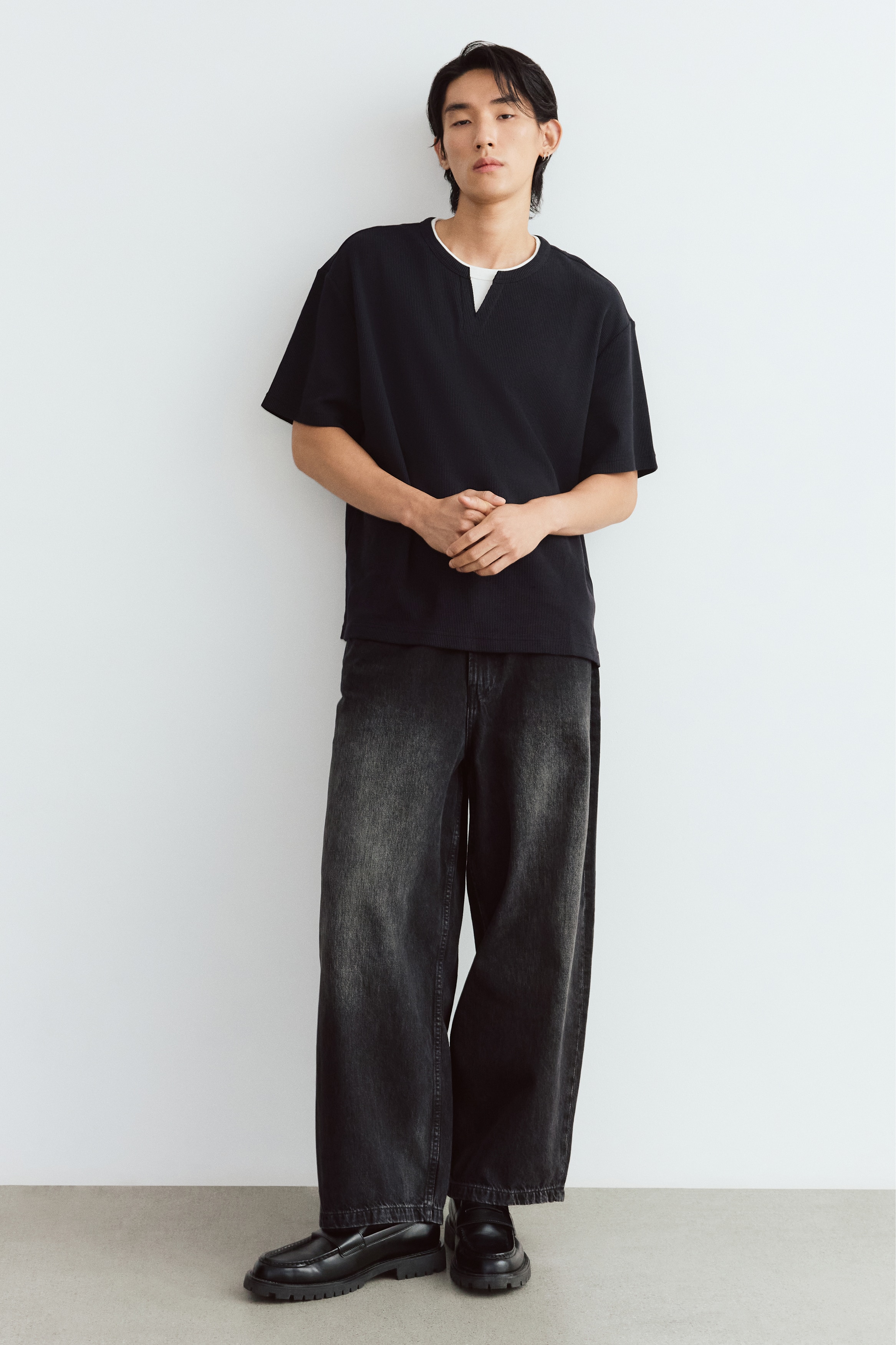 A black waffle-knit t-shirt shown from the front features a relaxed fit, short sleeves, and a layered collar design. The outer black neckline has a small V-neck slit that reveals an integrated off-white crew-neck underlayer.