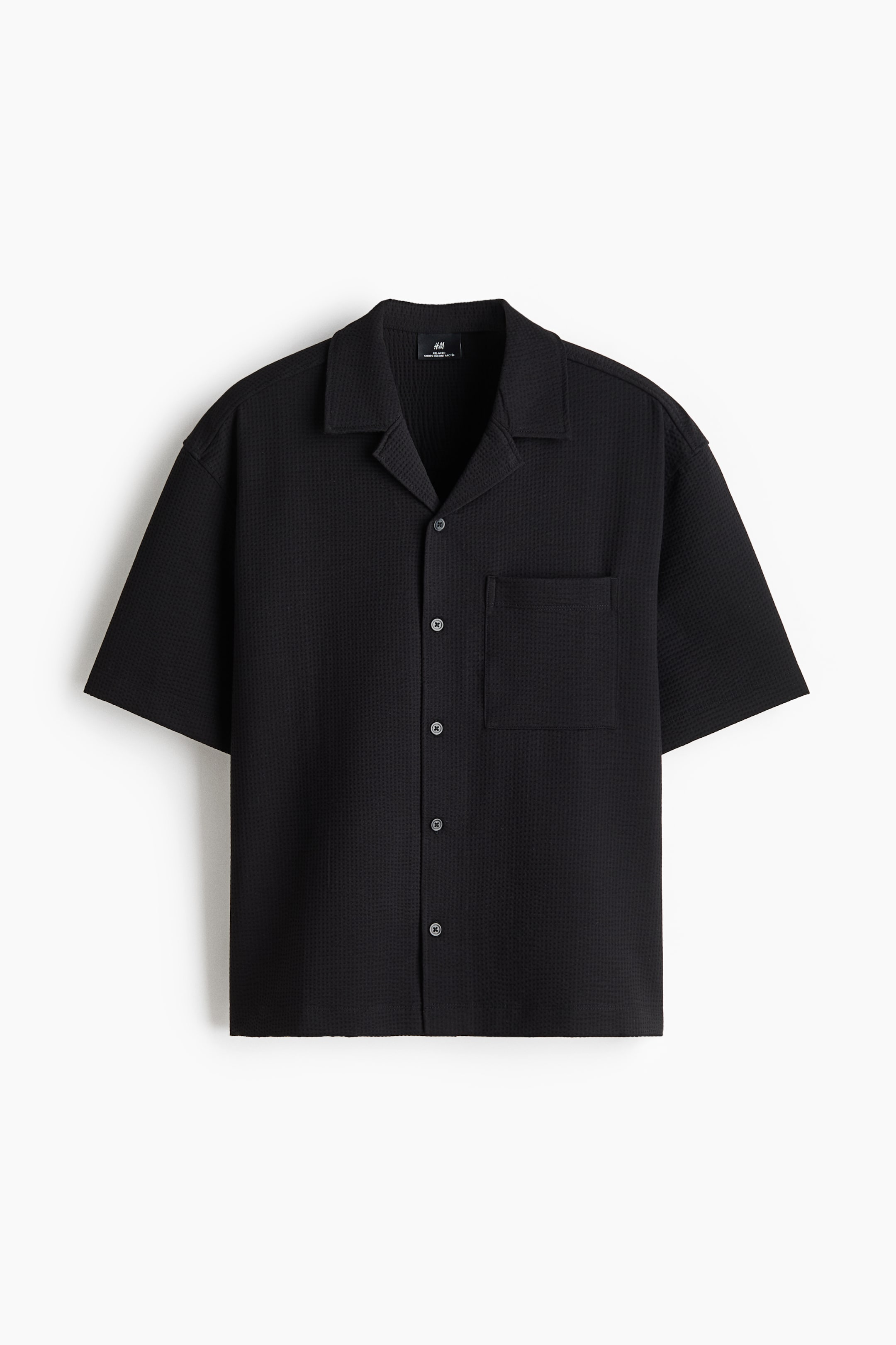 View larger image: A black, short-sleeve shirt in textured waffle-knit fabric is shown from the front, featuring a relaxed-fit silhouette, a resort collar, and a French front with button closures. It displays a single open chest pocket on the left side and a straight-cut hem.