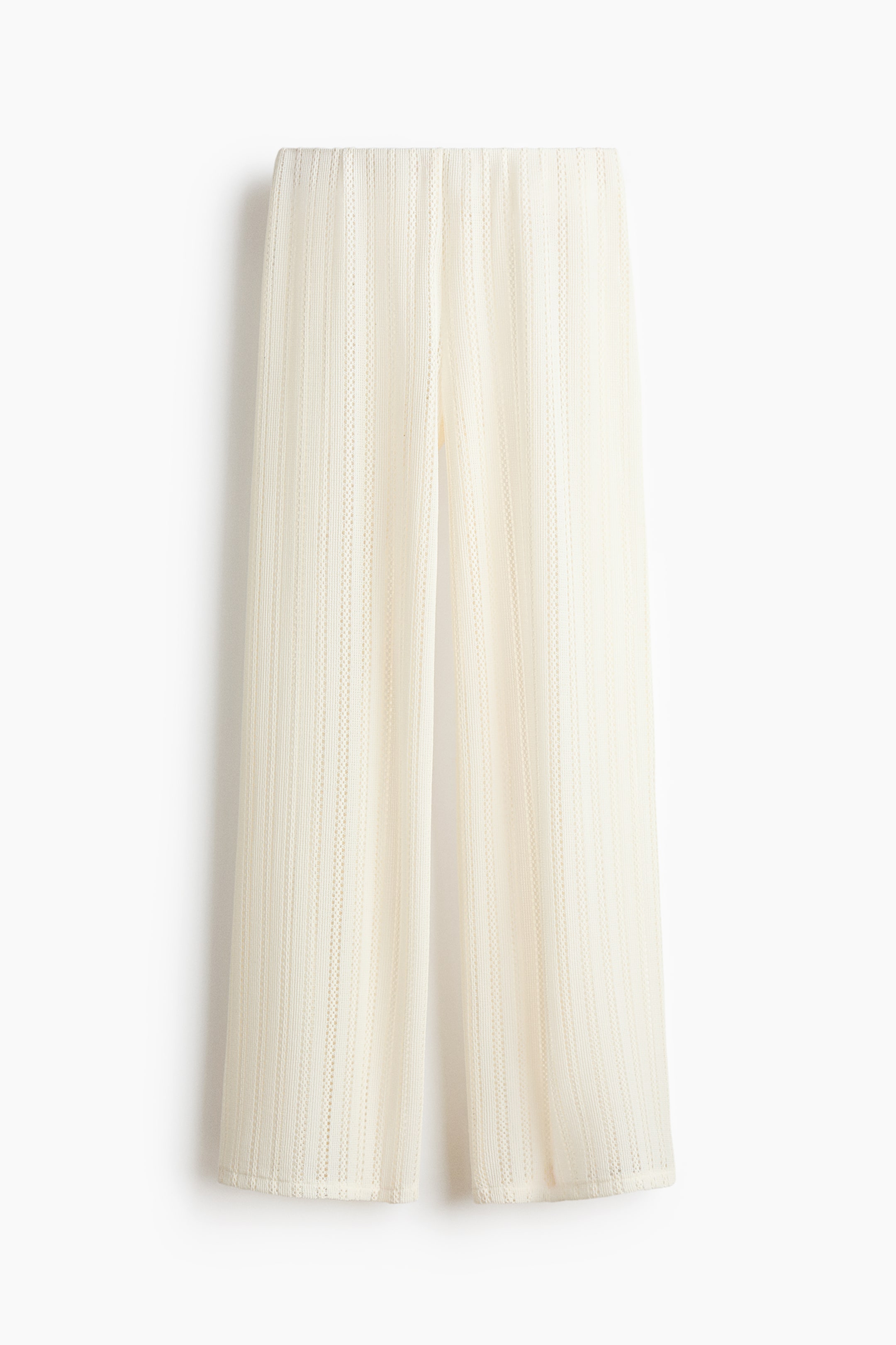 Ampliar la imagen: Pantalones de playa color crema presentados desde el frente, con cintura elástica y piernas rectas. Los pantalones están hechos de una tela de punto agujereada translúcida, mostrando un patrón vertical texturizado.