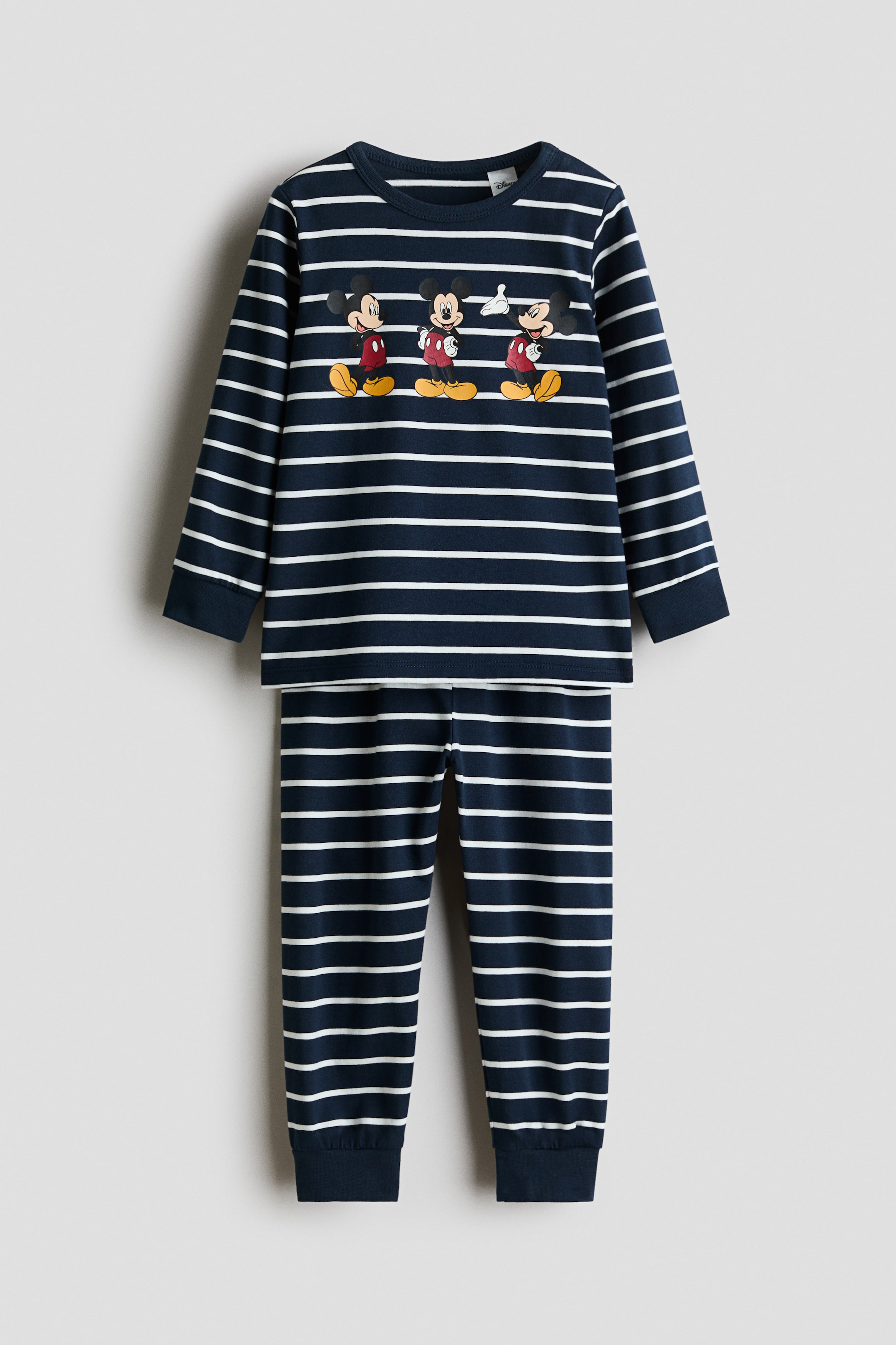 Größeres Bild anzeigen: Ein bedrucktes Baumwoll-Pyjama-Set ist von vorne zu sehen und präsentiert ein passendes langärmliges Oberteil und eine Hose im horizontalen Streifenmuster in Navy und Weiß. Das Oberteil zeigt drei aufgedruckte Mickey Mouse-Figuren über der Brust, und beide Teile verfügen über einfarbige, gerippte Bündchen in Navy.