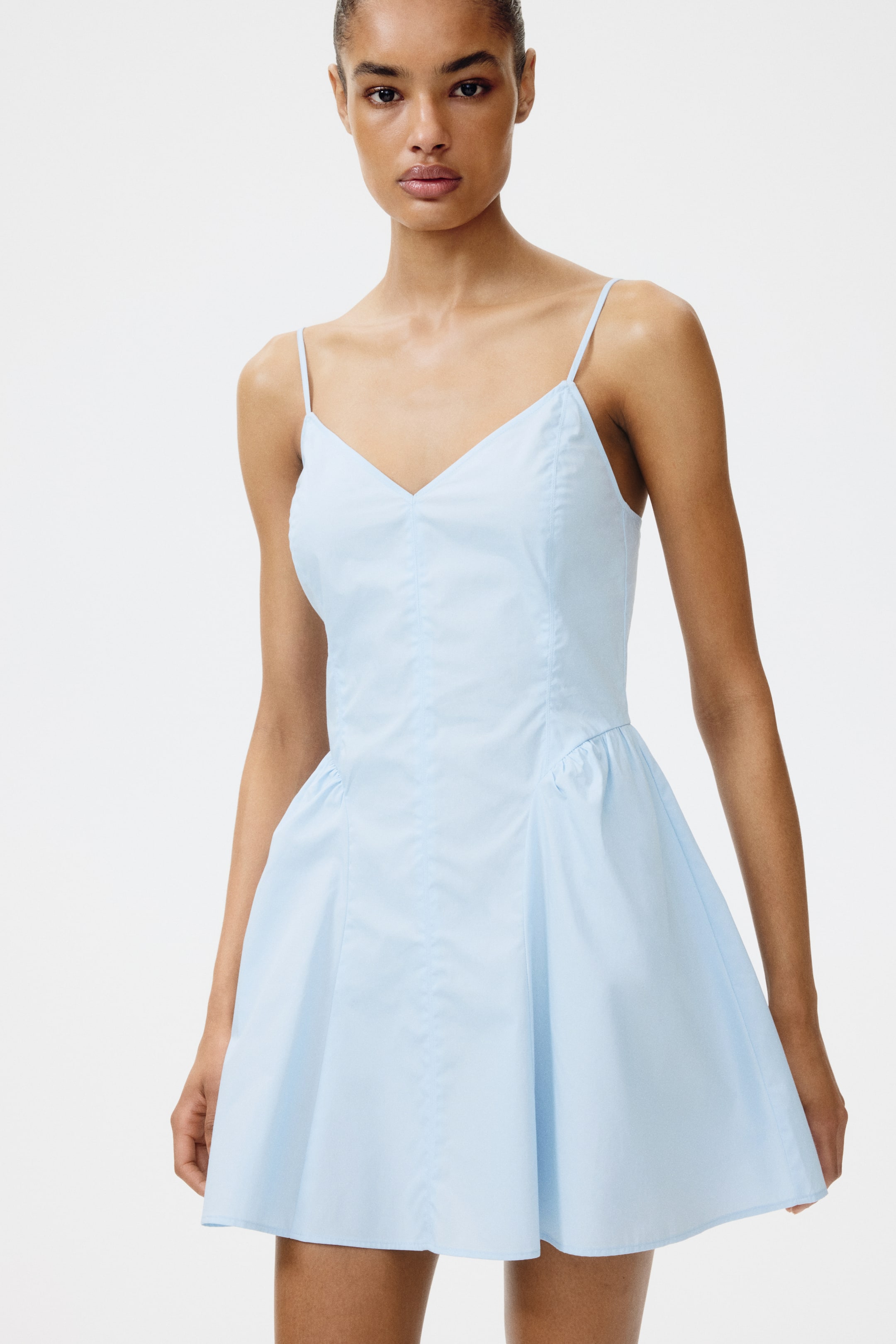 Agrandir l'image: Une robe courte bleu clair est présentée de face, avec un décolleté en V et de fines bretelles spaghetti. Elle est conçue avec un corsage ajusté, une taille froncée et une jupe évasée en ligne A.