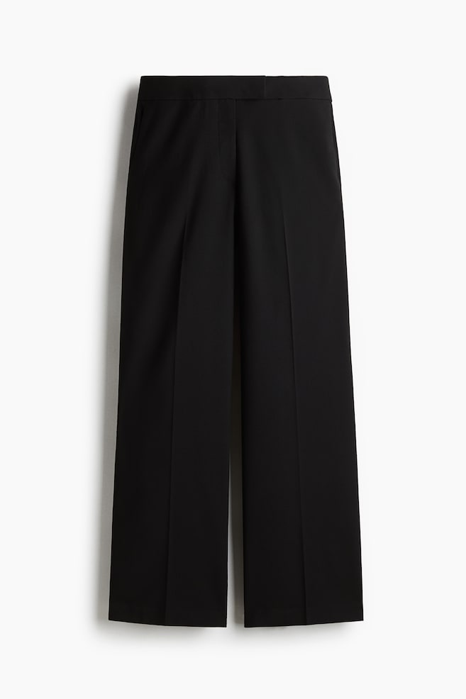 Schwarze, weit geschnittene Hosen werden von vorne gezeigt, mit einem flachen Bund, seitlichen Schlitztaschen und einer gepressten Mittelnaht, die an jedem Bein entlang verläuft. - 1