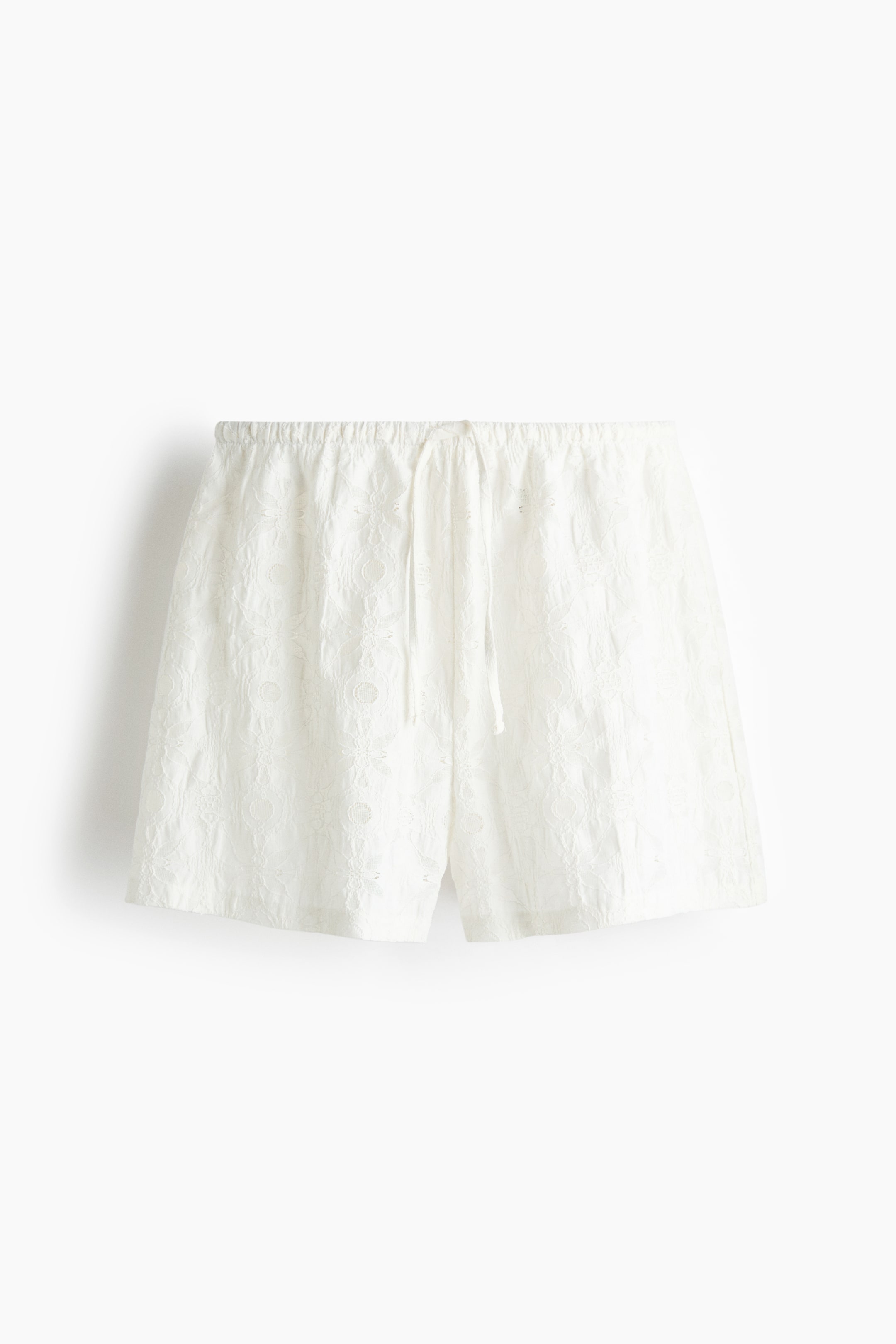 Ampliar la imagen: Los shorts blancos están colocados planos, mirando hacia adelante. Presentan un patrón de encaje de ojales por toda la prenda y una pretina elástica con un cordón blanco.