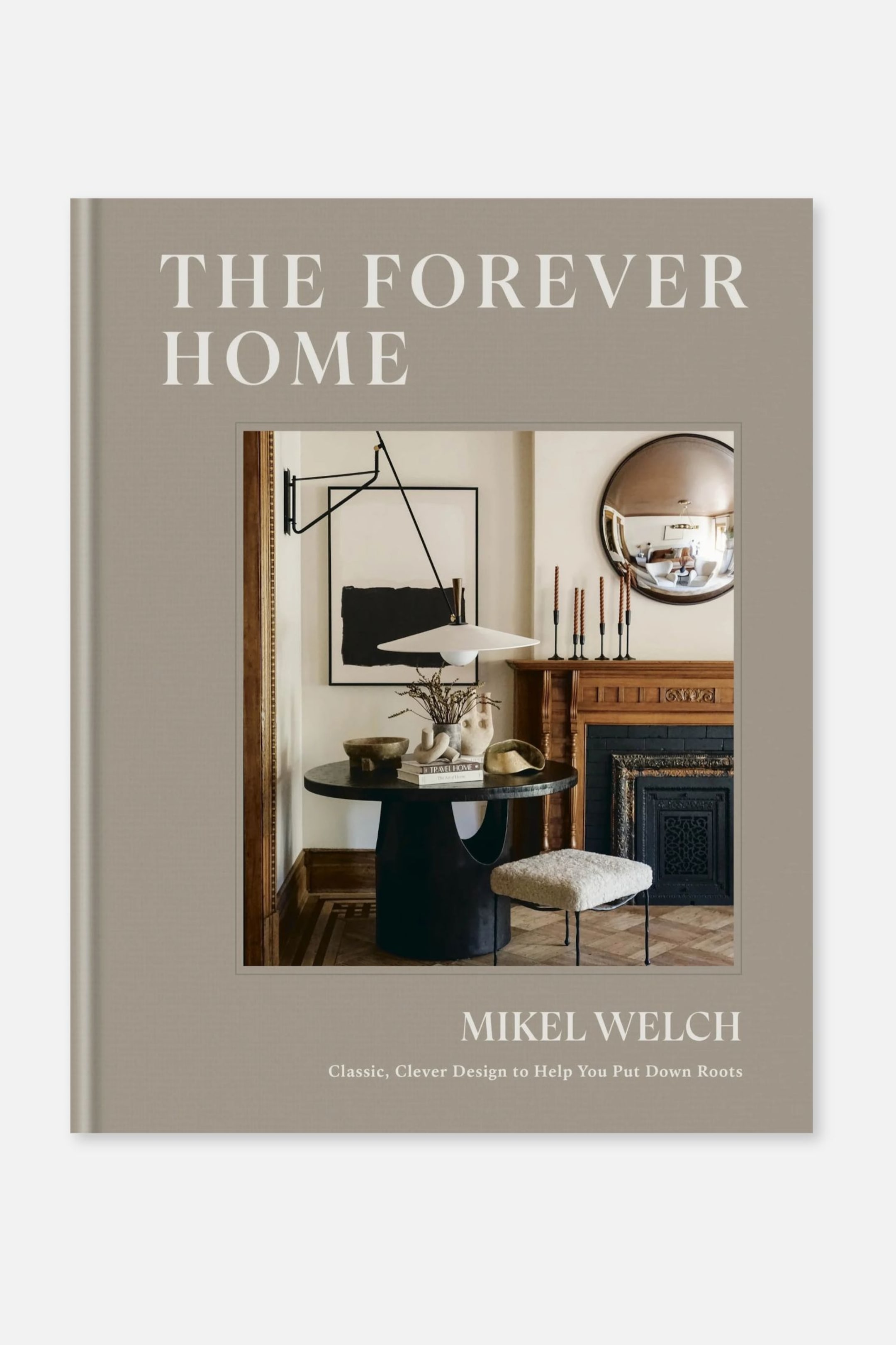 Größeres Bild anzeigen: Ein Hardcover-Buch mit dem Titel „THE FOREVER HOME“ von Mikel Welch zeigt einen taupefarbenen Einband mit weißer Serifenschrift. Auf dem Titelblatt befindet sich ein zentrales rechteckiges Eingangsbild eines stilvoll eingerichteten Innenraums mit einem dunklen Sockeltisch, einem Kamin und einem runden Spiegel.