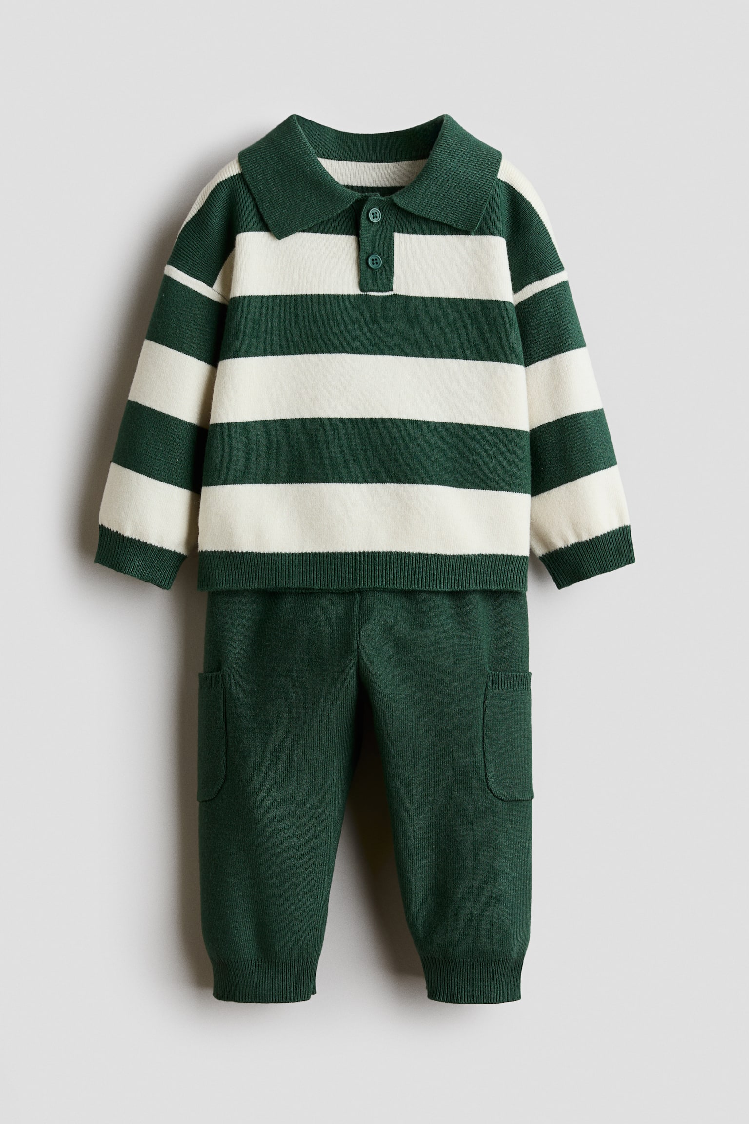 A front-facing knit sweater and pants set showcases a green and cream horizontally striped sweater paired with solid green pants. The sweater features a collar, a two-button placket, dropped shoulders, and ribbed cuffs and hem, while the pants display patch pockets on the legs and ribbed ankle cuffs.