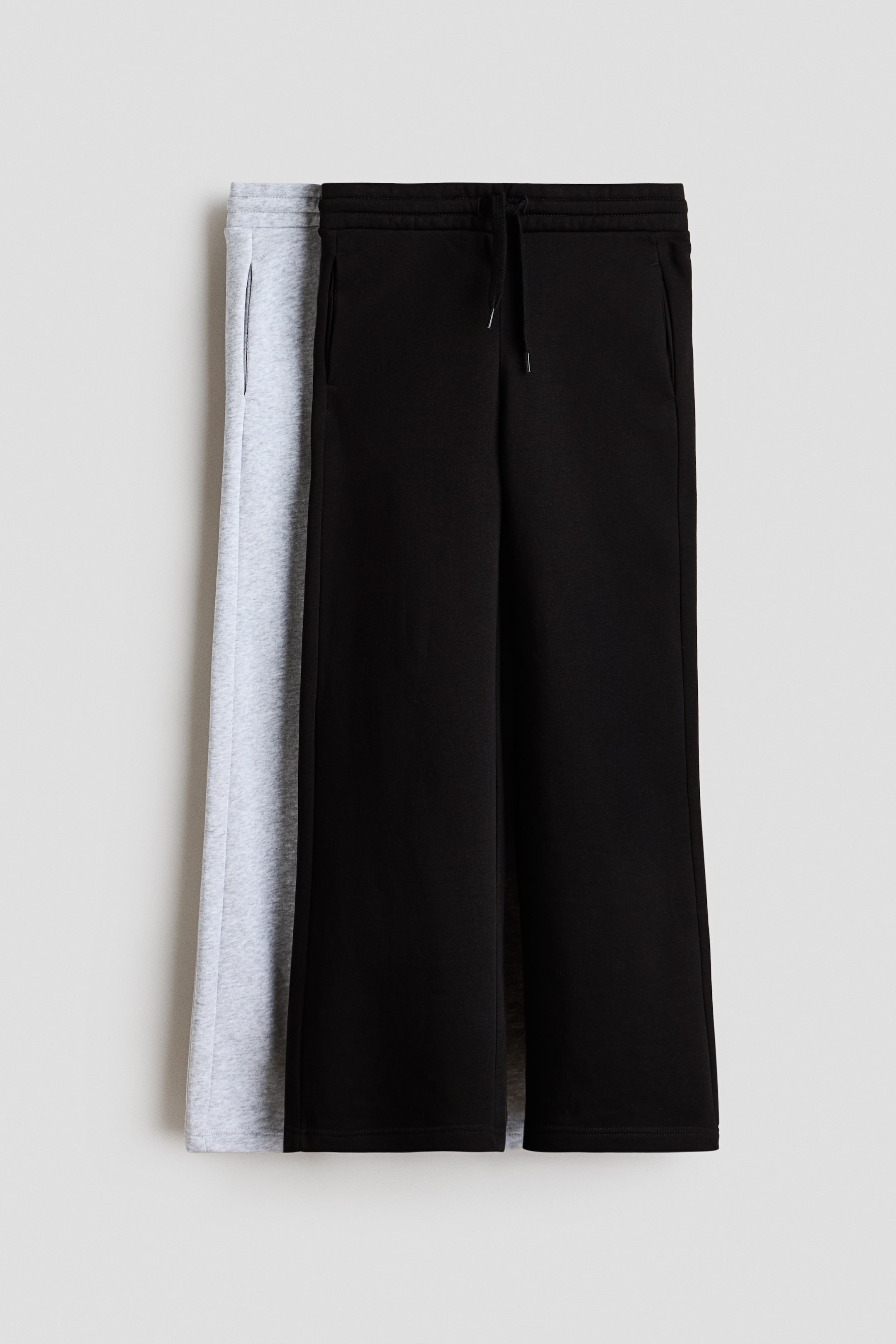 View larger image: Two pairs of joggers are laid flat in a front view, with a black pair overlapping a light grey marl pair. Both pairs feature fleece sweatshirt fabric, an elasticated drawstring waist with a visible drawstring, discreet side pockets, and straight legs.
