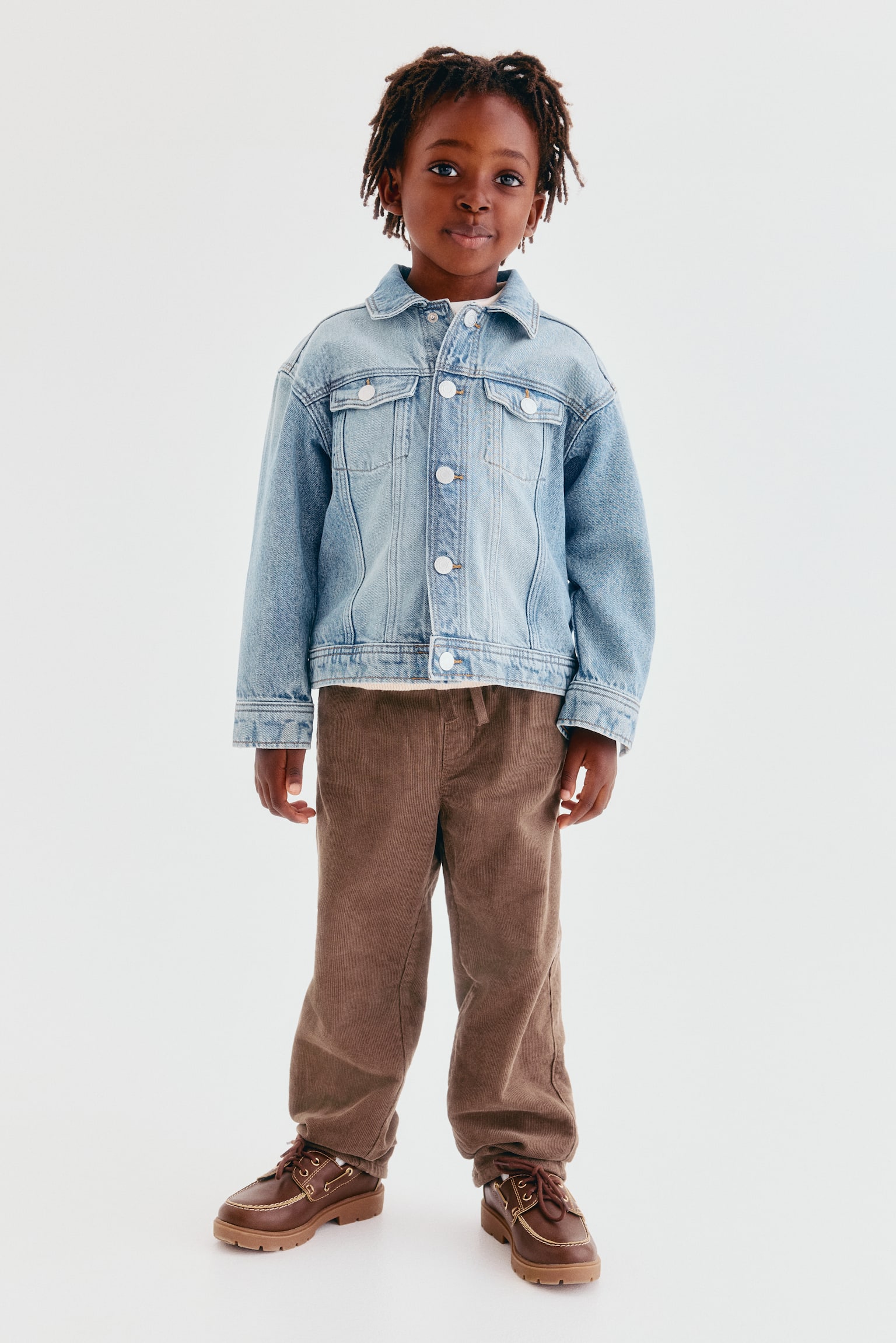 Soft brown corduroy trousers are shown from the front, featuring an elasticated drawstring waist, a faux fly and side slash pockets, with a loose fit through the hip and thigh and legs gently tapering towards the hem. - 1
