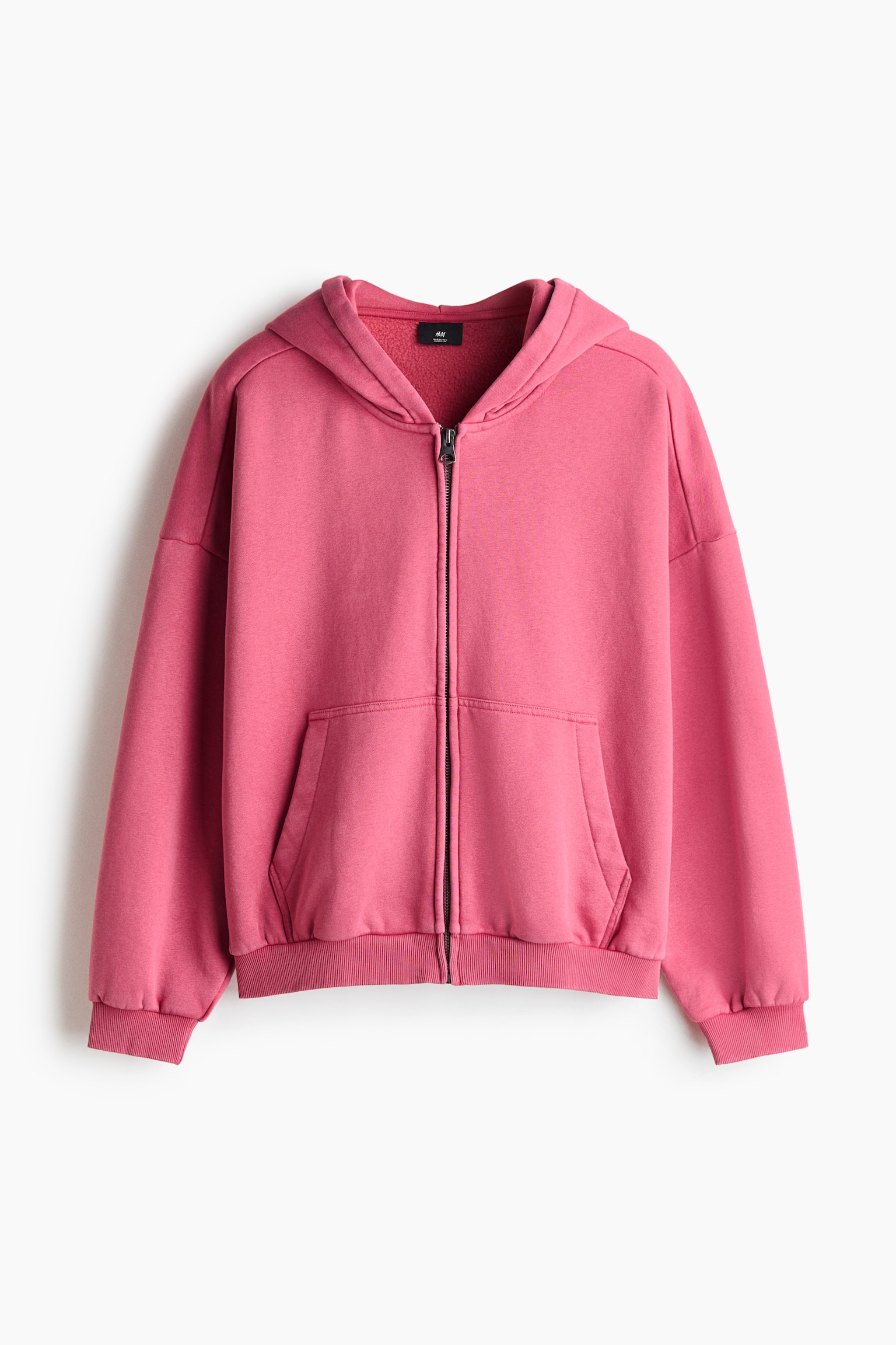 A pink zip-up hoodie is hanging and facing the front, featuring a relaxed fit with dropped shoulders, long sleeves and a full-length centre zip. The hoodie features a split kangaroo pocket at the waist, along with ribbed cuffs and a ribbed hem.