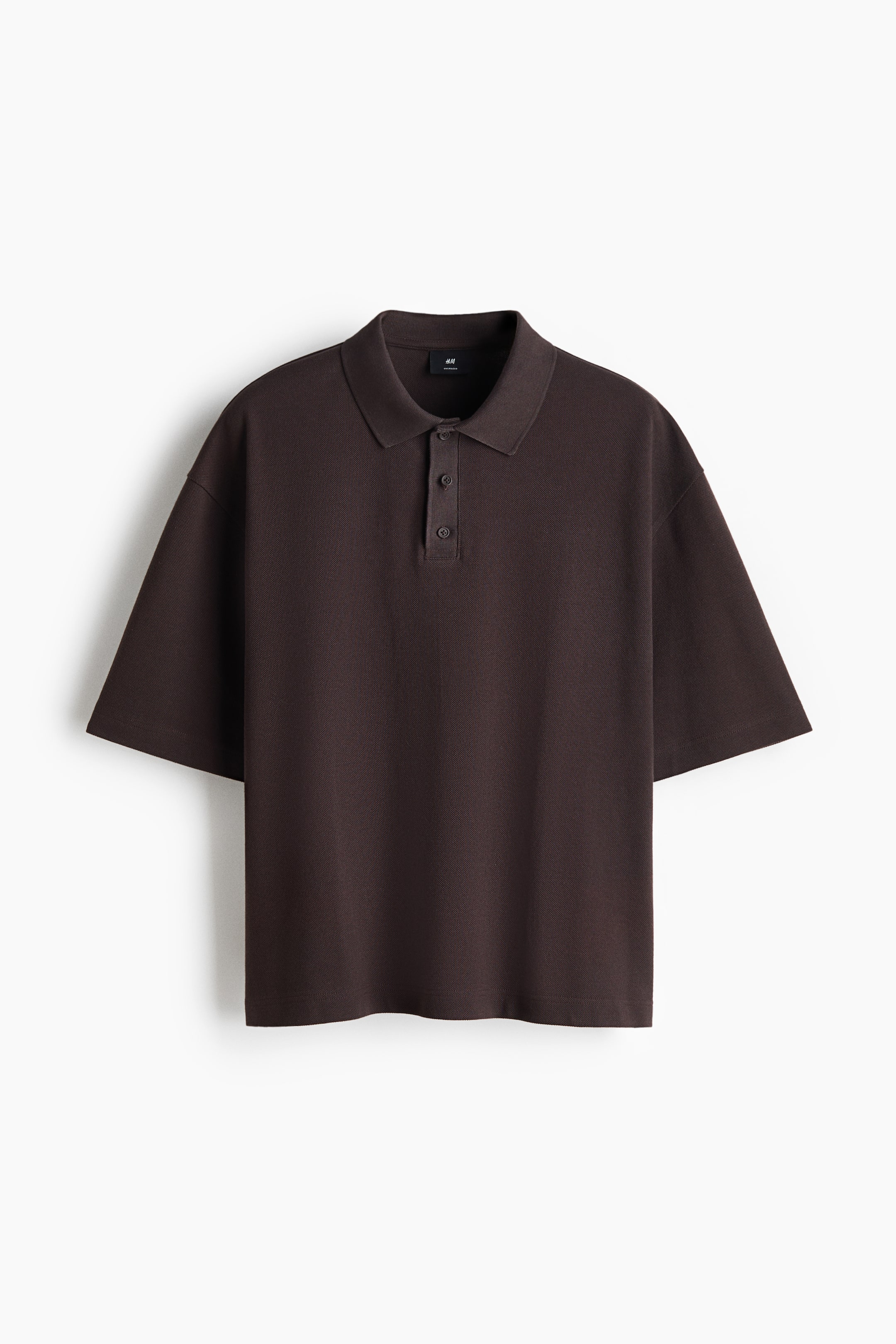 Größeres Bild ansehen: Dieses dunkelbraune Poloshirt zeigt von vorne eine lässige, oversized Passform mit überschnittenen Schultern und weiten, bis zum Ellbogen reichenden Ärmeln. Es präsentiert einen klassischen Flachstrickkragen mit einer Drei-Knopf-Leiste und einem klaren, geraden Saum.