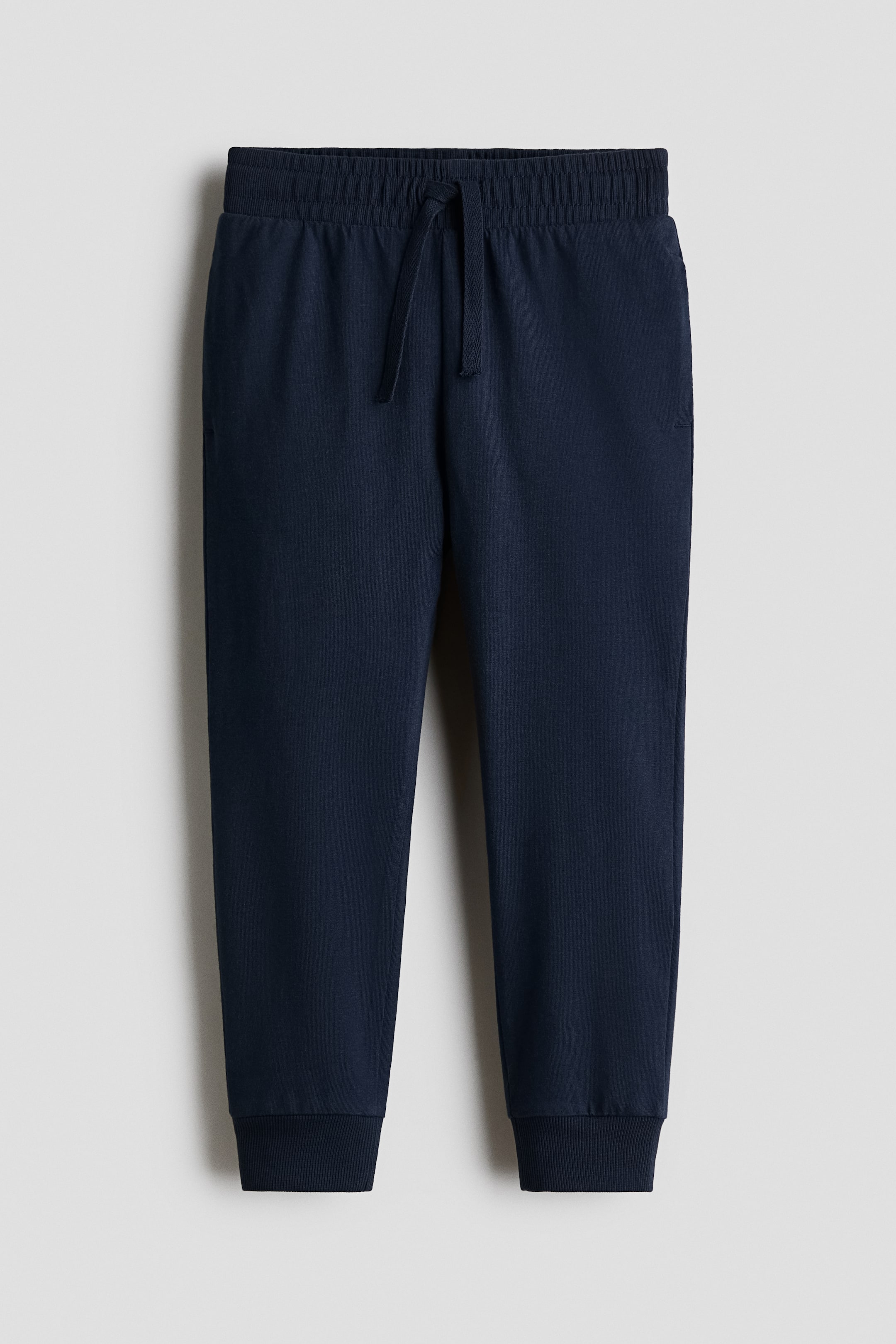 View larger image: Navy blue sweatpants featuring an elasticated, ribbed waistband with a drawcord, and ribbed cuffs at the ankles.