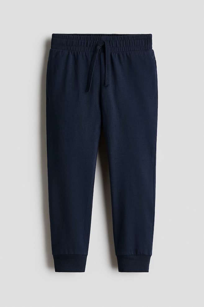 Navy blue sweatpants feature an elasticated, ribbed waistband with a drawcord, and ribbed cuffs at the ankles. - 1