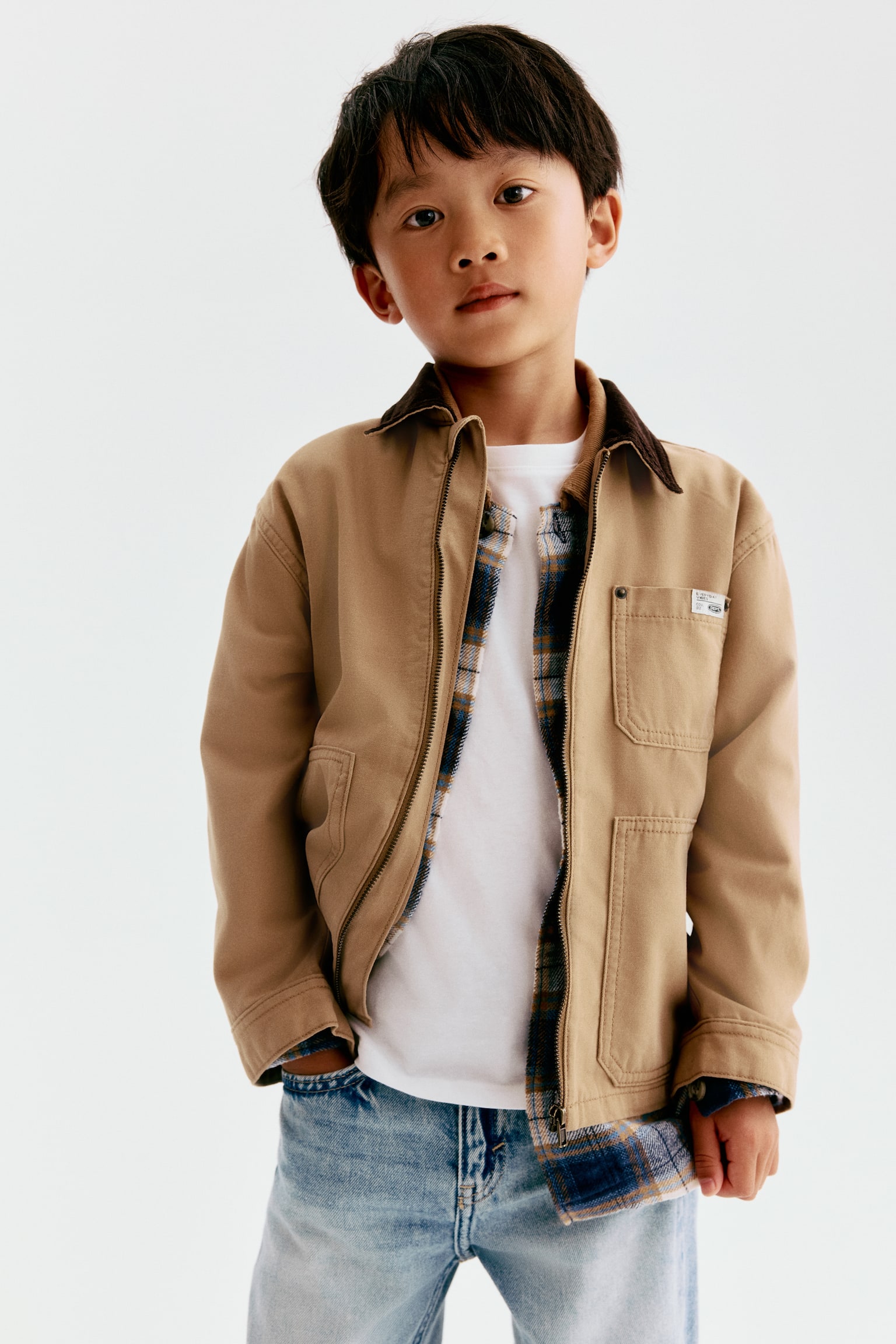 The oversized overshirt is shown from the front, featuring a tan soft cotton twill fabric with a dark brown cotton corduroy turn-down collar. It is displaying a full-length front zipper, dropped shoulders, and multiple patch pockets on the chest and lower front. - 1