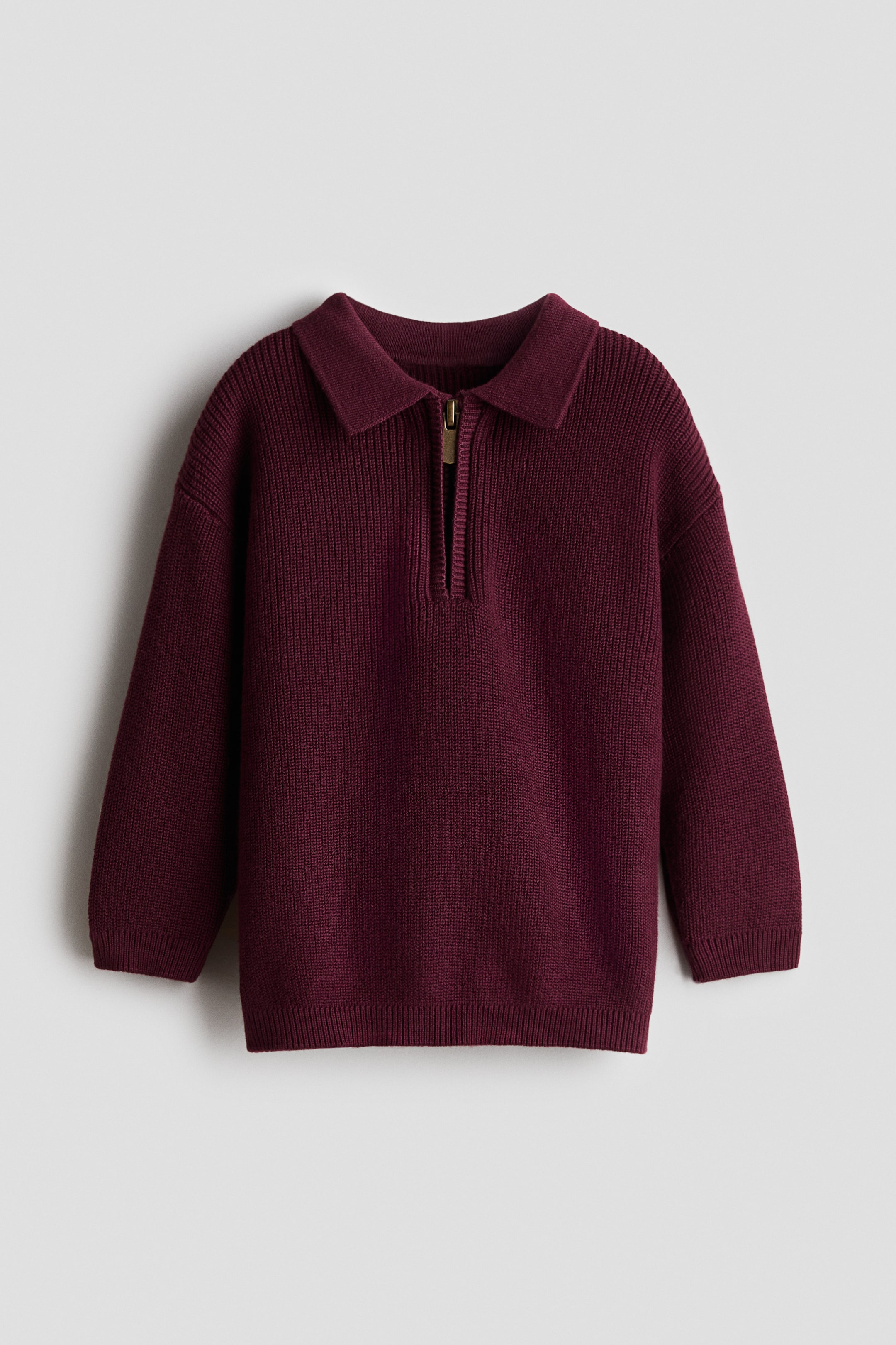 Ver imagen más grande: Un jersey polo burdeos se muestra desde el frente, con una textura de punto acanalado, un cuello, una cremallera en tono dorado en la parte superior, hombros caídos, puños acanalados y un dobladillo acanalado.