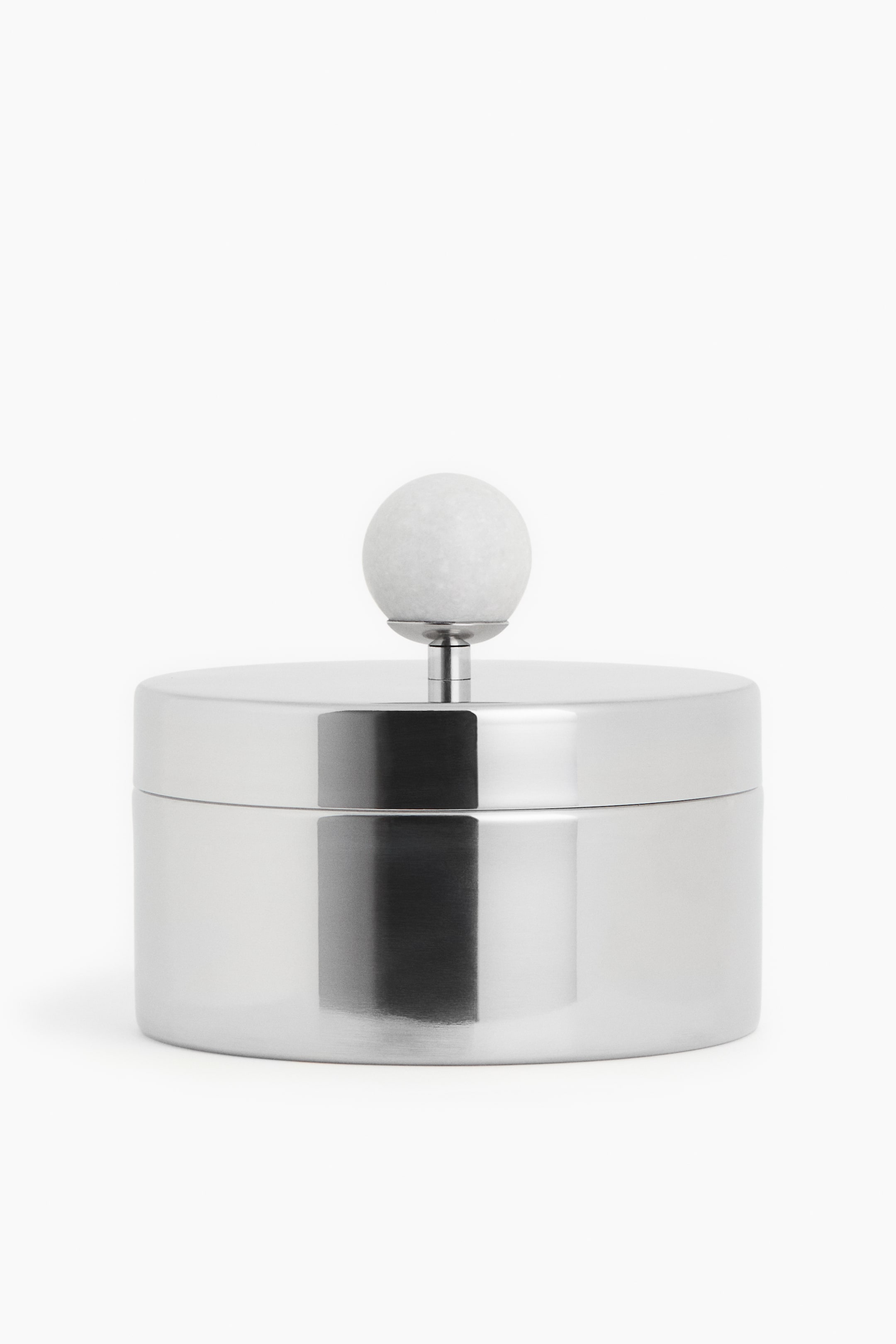 View larger image: A polished silver-toned metal container is displayed from the front. It showcases a cylindrical body and a flat lid, with a white spherical marble knob elegantly rising from the center of the lid on a slender metal stem.