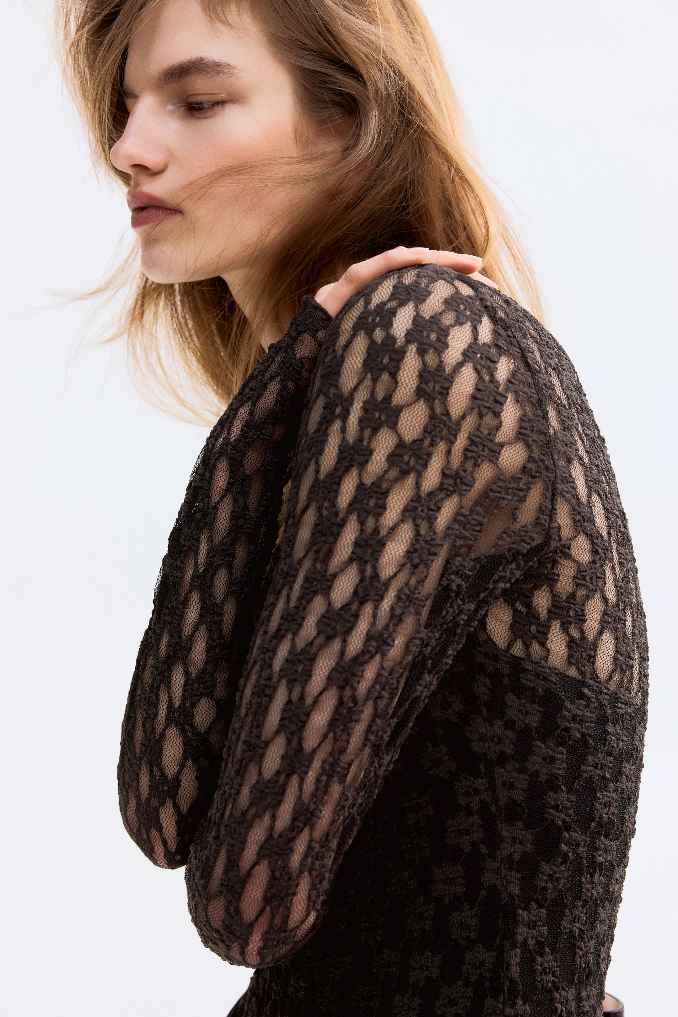 View larger image: A dark brown long-sleeved top features a raised textural openwork pattern across its sleeves and shoulder, viewed from a side angle.