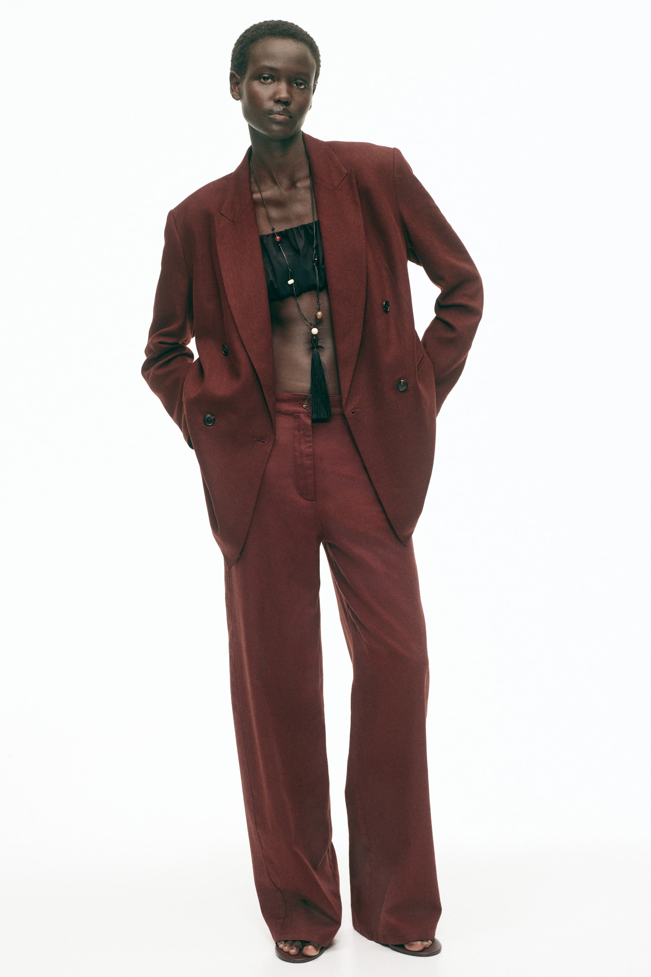 View larger image: Introducing a deep red double-breasted blazer, showcasing notch lapels, broad shoulders, and dual rows of dark buttons. Styled open over a black bandeau top, it is paired with matching high-waisted, wide-leg trousers for a chic ensemble.