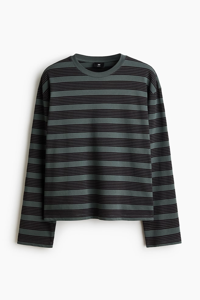 A boxy, long-sleeve T-shirt featuring dark green and black horizontal stripes is hanging facing forward. It is displaying a relaxed silhouette with a round ribbed neckline, dropped shoulders, and a straight-cut hem. - 1