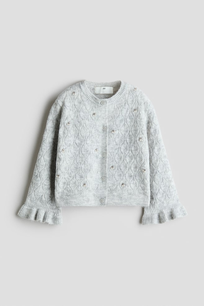 A light grey knit cardigan is shown from the front, featuring a diamond-patterned textured knit embellished with scattered small faux pearls. The design includes a button-down front with grey buttons, a ribbed crew neck, and long sleeves with flared, ruffled cuffs. - 1