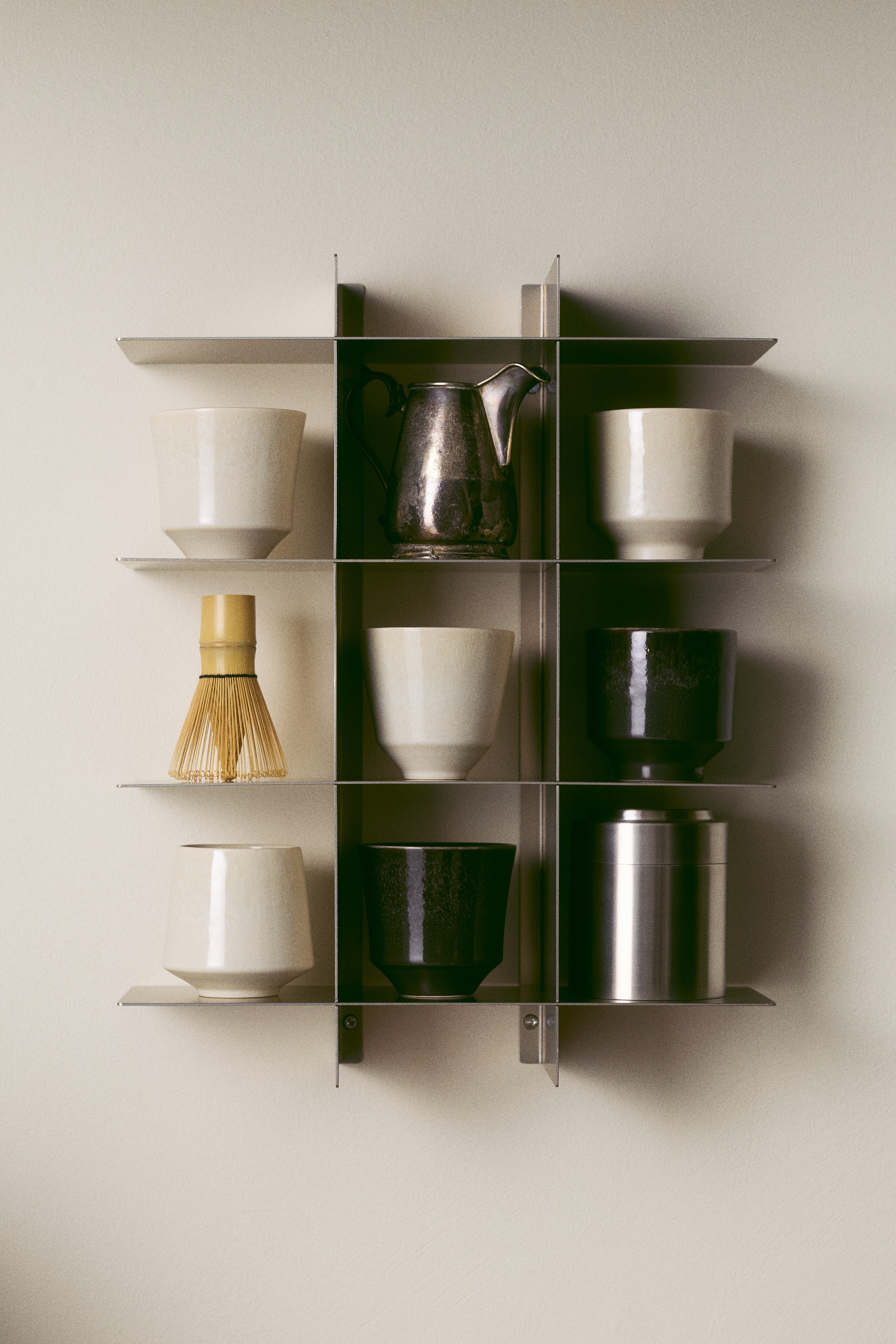 Una estanterÃ­a metÃ¡lica de pared en color beige champÃ¡n muestra un diseÃ±o minimalista en rejilla desde el frente. Presenta cuatro baldas horizontales finas y planas que se cruzan con dos soportes verticales de sujeciÃ³n, con orificios circulares de montaje visibles cerca de la parte superior e inferior.
