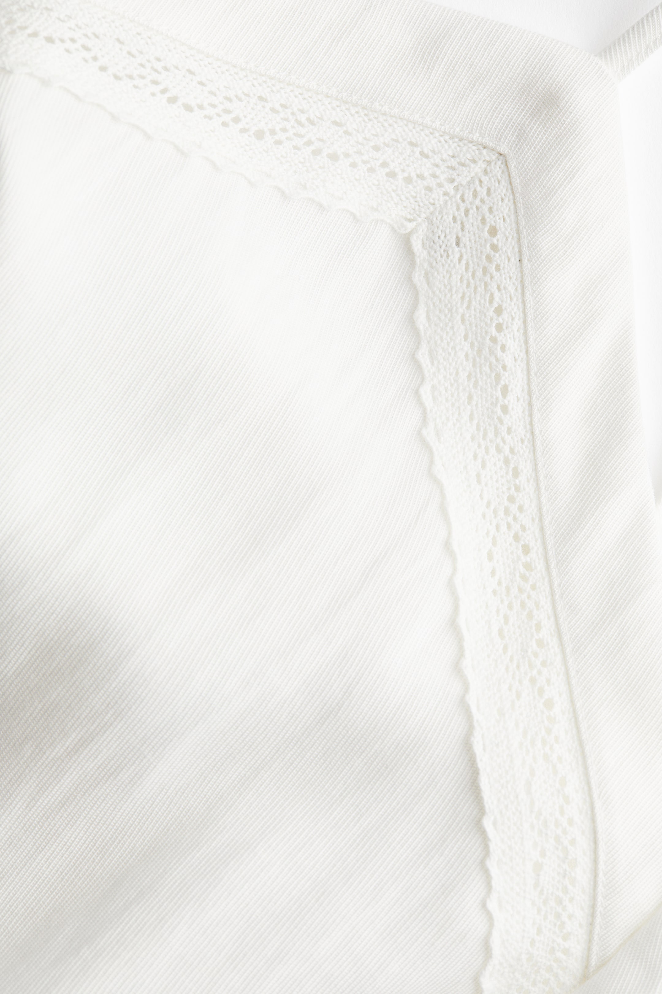 Xem ảnh lớn hơn: Một loại vải trắng với kết cấu chéo tinh tế có viền ren tinh xảo, thoáng khí dọc theo cạnh trên và cạnh phải, tạo thành một góc.