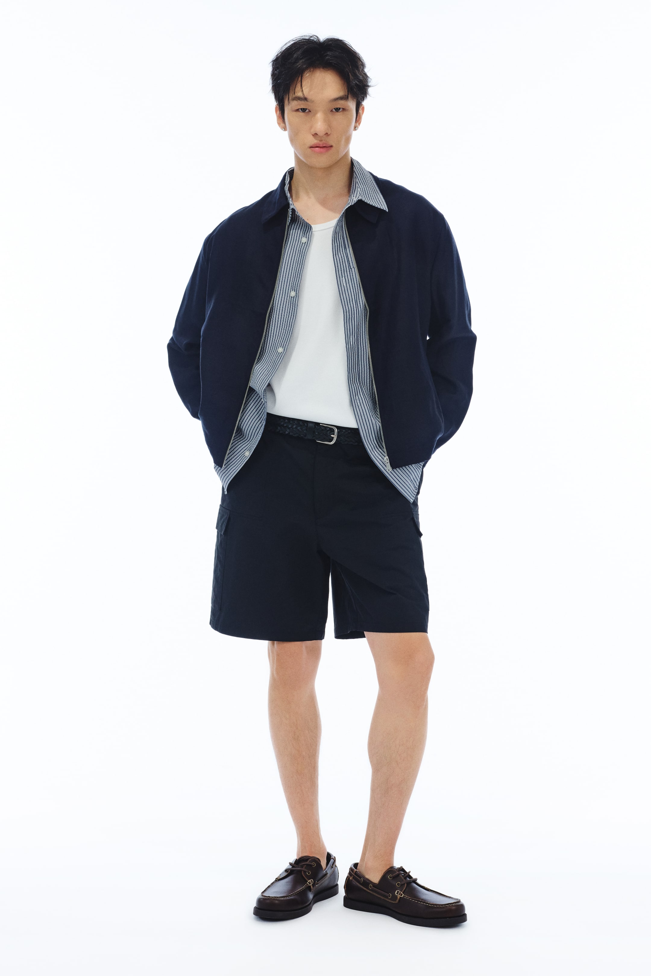 View larger image: "The model is sporting dark blue cargo shorts that offer a relaxed fit, complete with slanted side pockets and patch leg pockets with flaps. Complementing the shorts is a braided black belt."