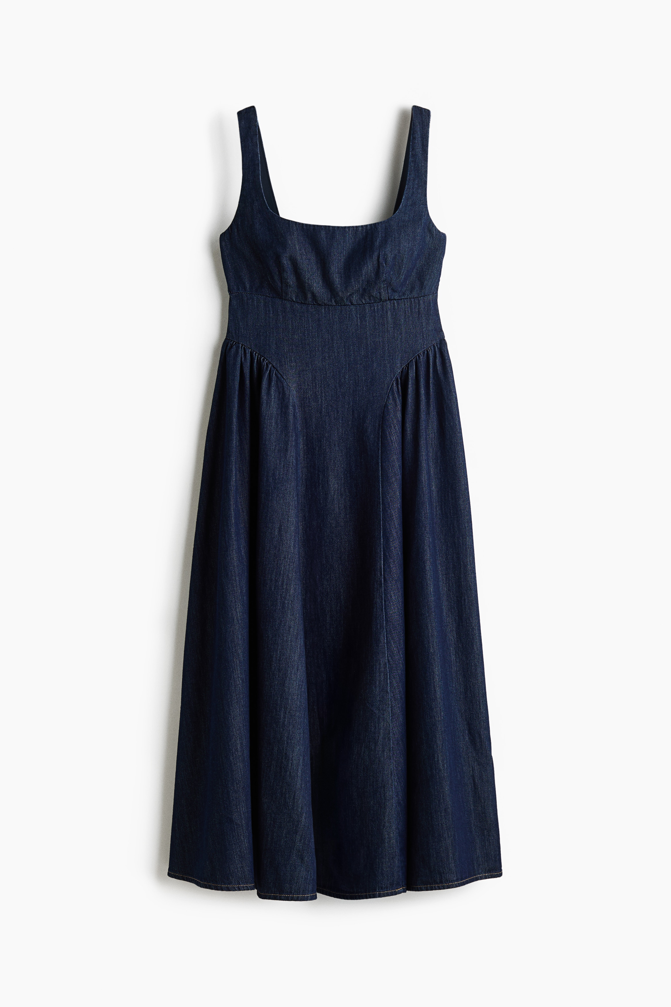 The model is wearing a dark blue, lightweight denim midi dress. The dress features a square ballerina neckline, wide shoulder straps, a horizontal seam below the bust, and a flared skirt with curved, gathered seams over the hips.