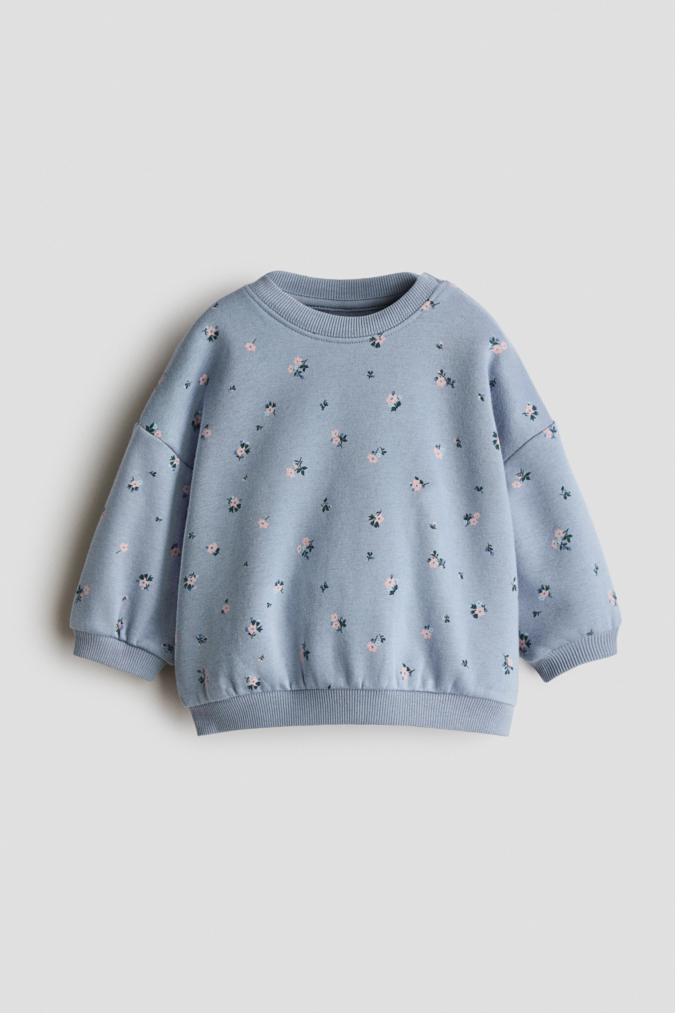View larger image: A light blue printed sweatshirt is facing forward, featuring a scattered floral pattern with pink blossoms and green leaves. It is displaying a ribbed crew neck, long sleeves with ribbed cuffs, and a ribbed hem.