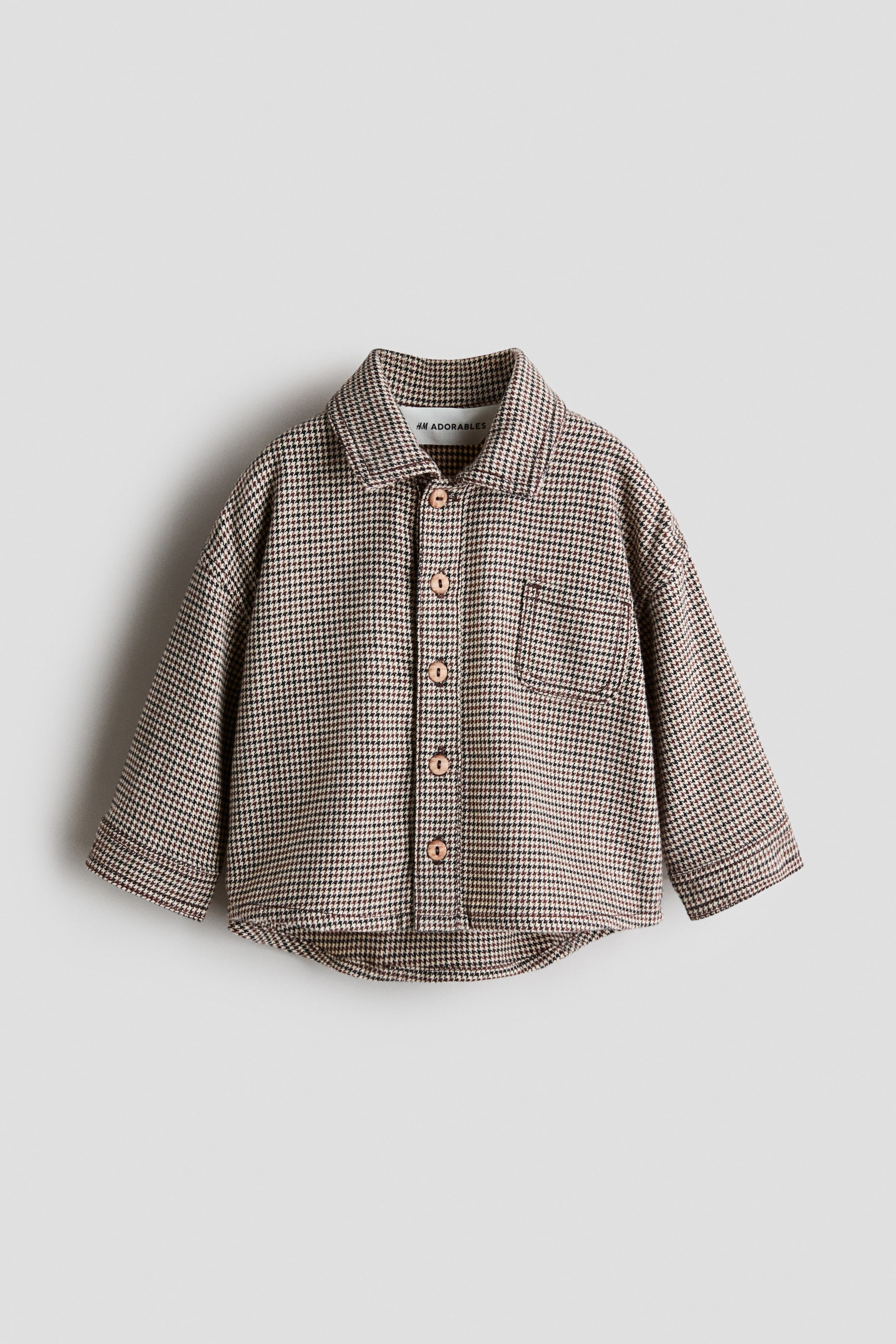 View larger image: A brown and black houndstooth check shirt is laid flat, facing front. It features a spread collar, a full button-up front with light brown buttons, and a single patch pocket on the left chest. The shirt showcases long sleeves and a curved hem.