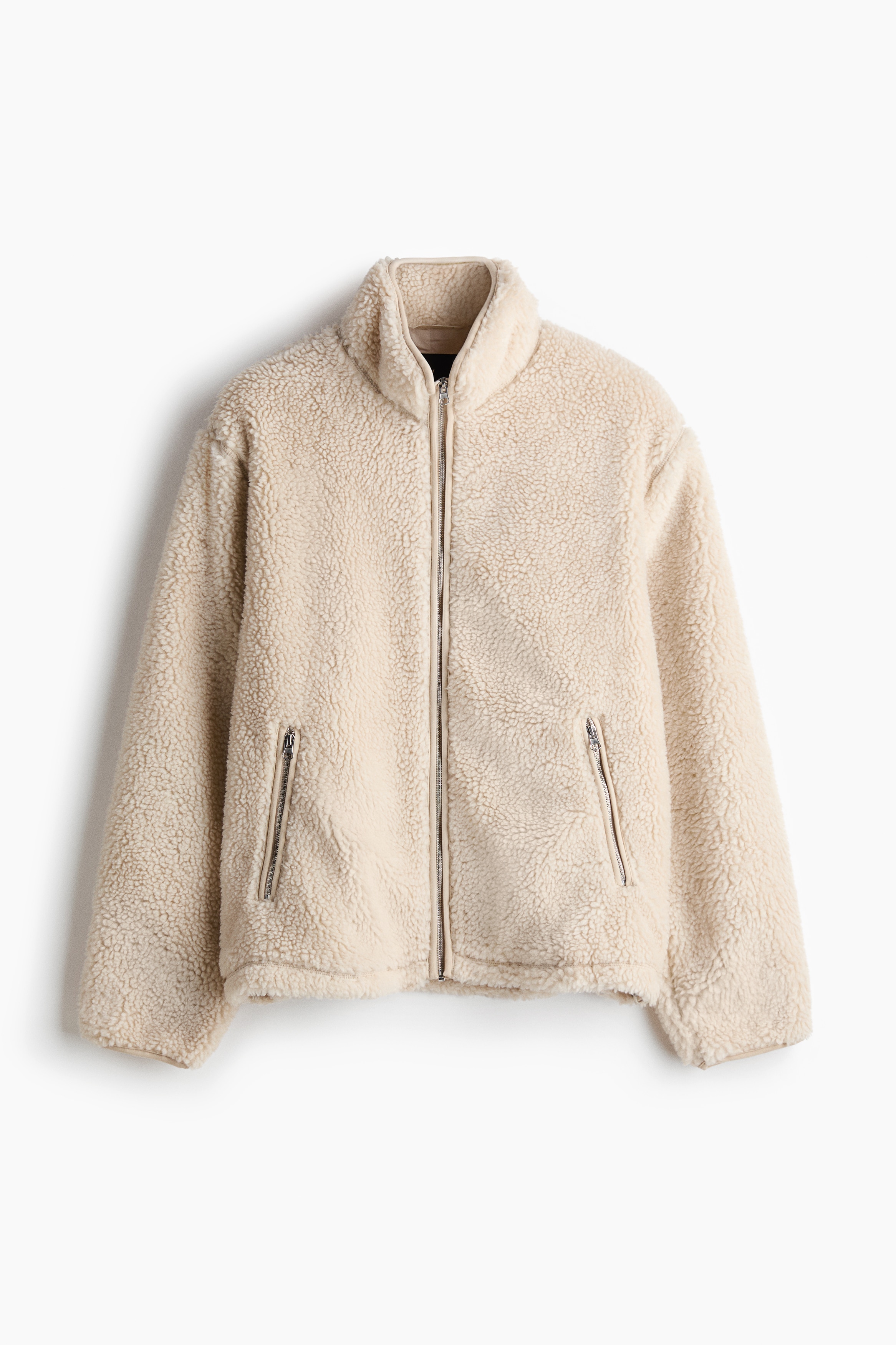 Une veste en teddy fleece couleur crÃ¨me est portÃ©e ouverte par le mannequin, mettant en valeur son col montant, sa fermeture zippÃ©e sur le devant et ses Ã©paules tombantes. La veste est superposÃ©e Ã  un pull en maille bleu foncÃ© et Ã  une chemise bleu clair Ã  col.