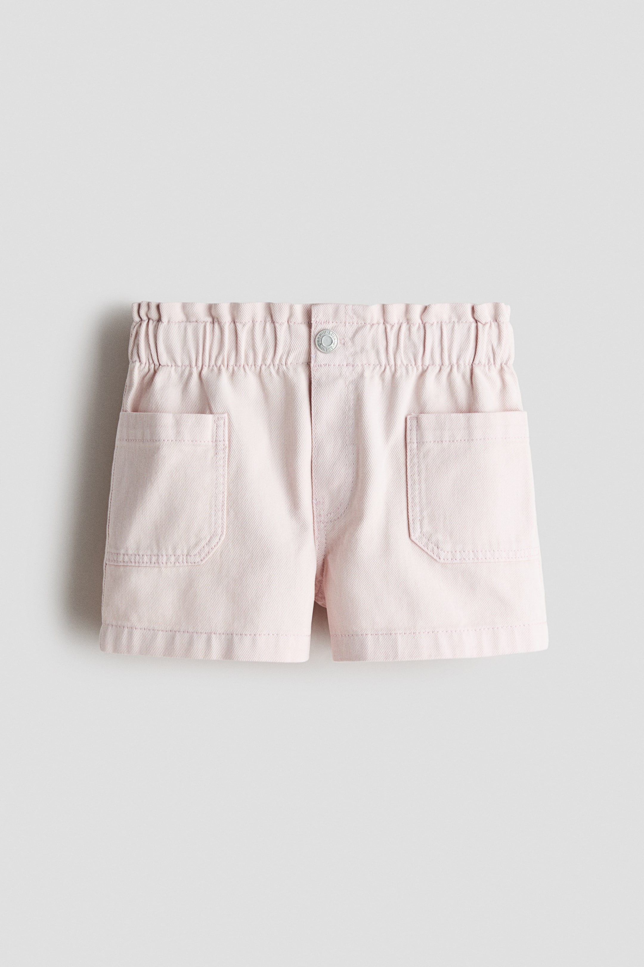 View larger image: Loose-fit shorts in washed cotton denim are displaying a light pink color. The FRONT features an elasticated, paper bag waist, a fake fly with a central press-stud, and two diagonal front pockets.