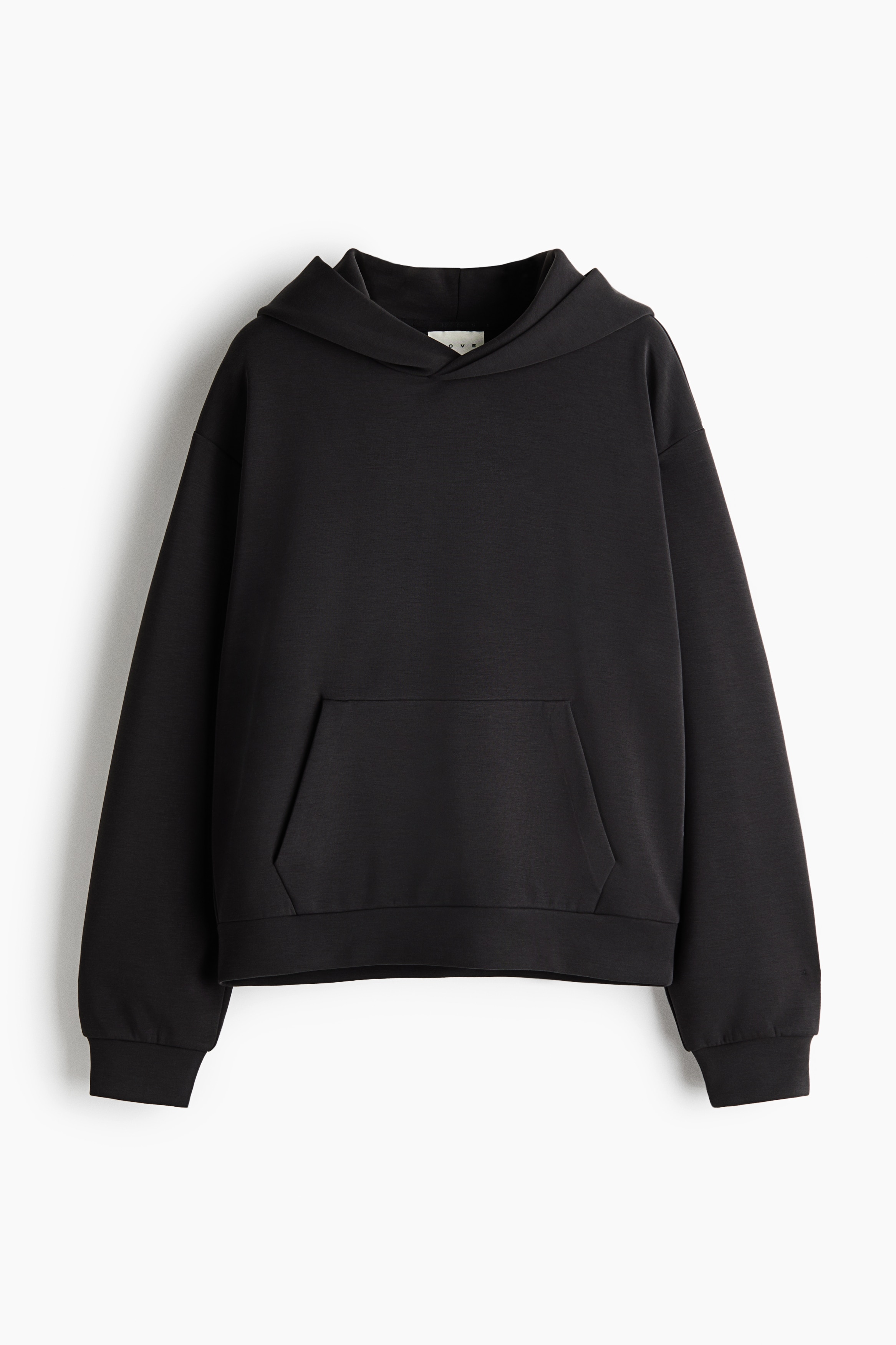 An oversized, dark grey activewear hoodie featuring a lined wrap hood, dropped shoulders, and a front kangaroo pocket is worn by the model. The hoodie is layered over a black high-neck top and styled with black leggings.