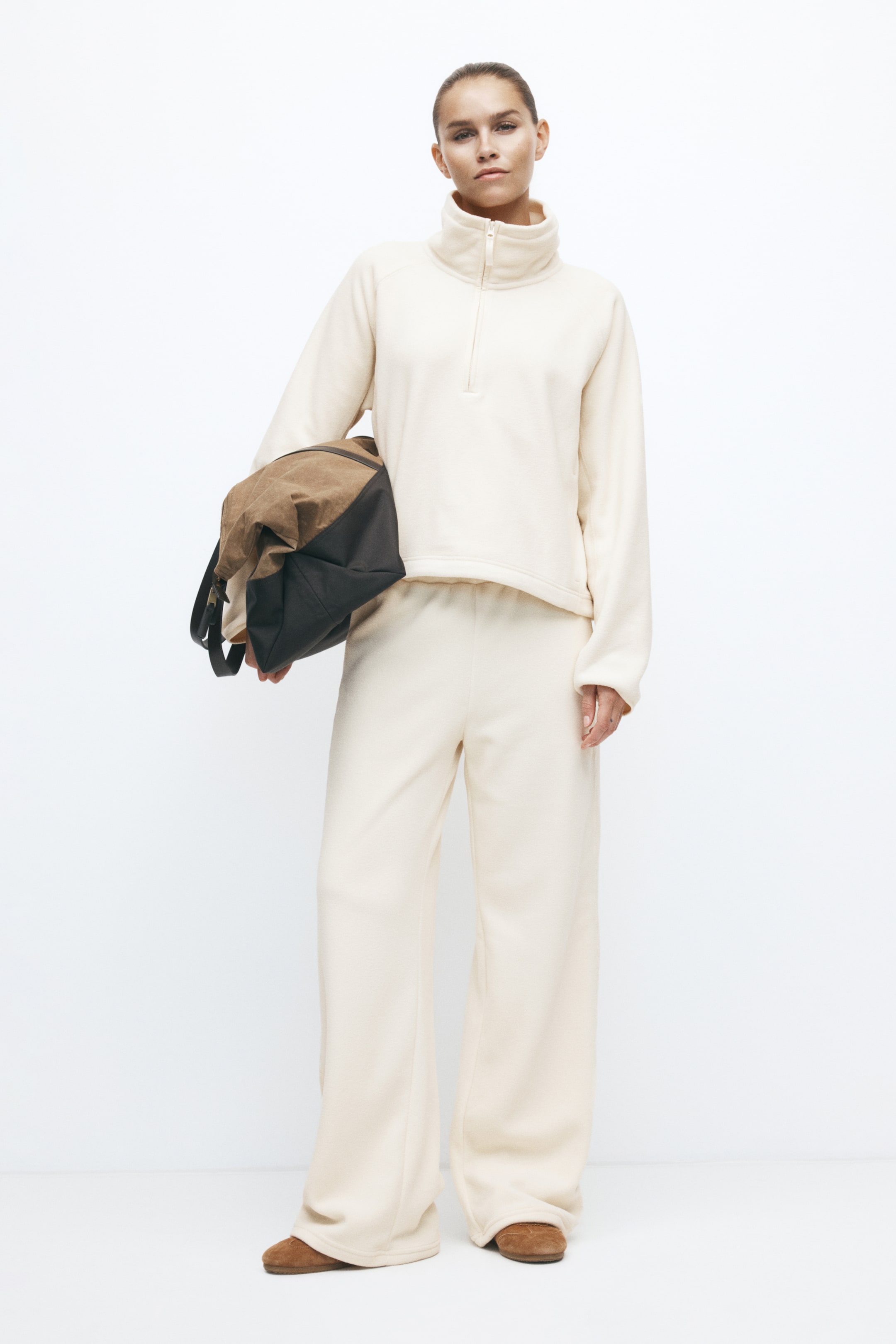 Agrandir l'image: Un jogging coupe décontractée en molleton blanc cassé est porté par le mannequin, avec une taille élastiquée et une silhouette à jambe large. Le jogging est associé à un pull molleton assorti blanc cassé, avec un sac marron et noir porté sous le bras.