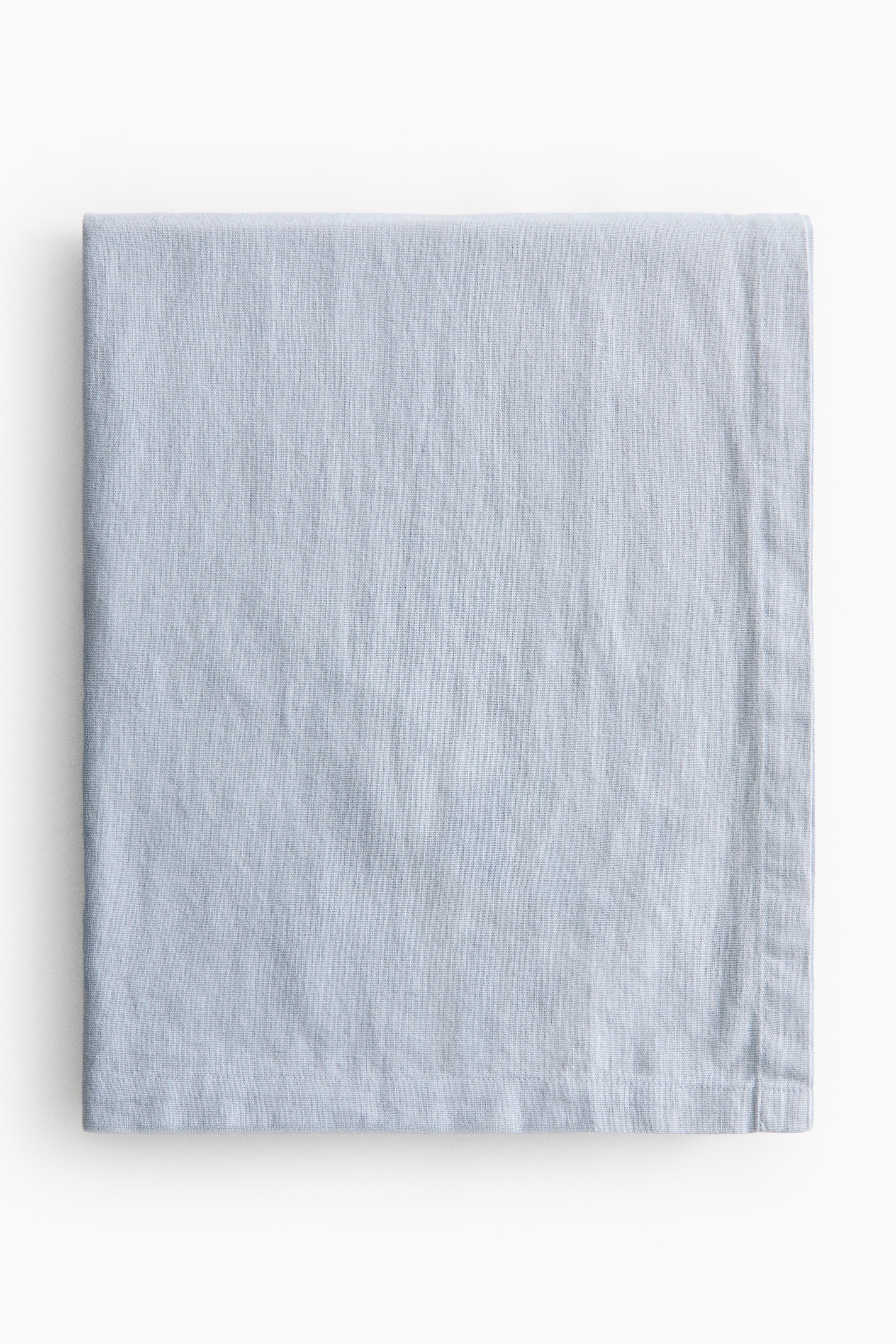 View larger image: A light blue tablecloth is folded, showcasing a woven texture with gentle creasing. It features a 1-inch folded hem along its visible edges.