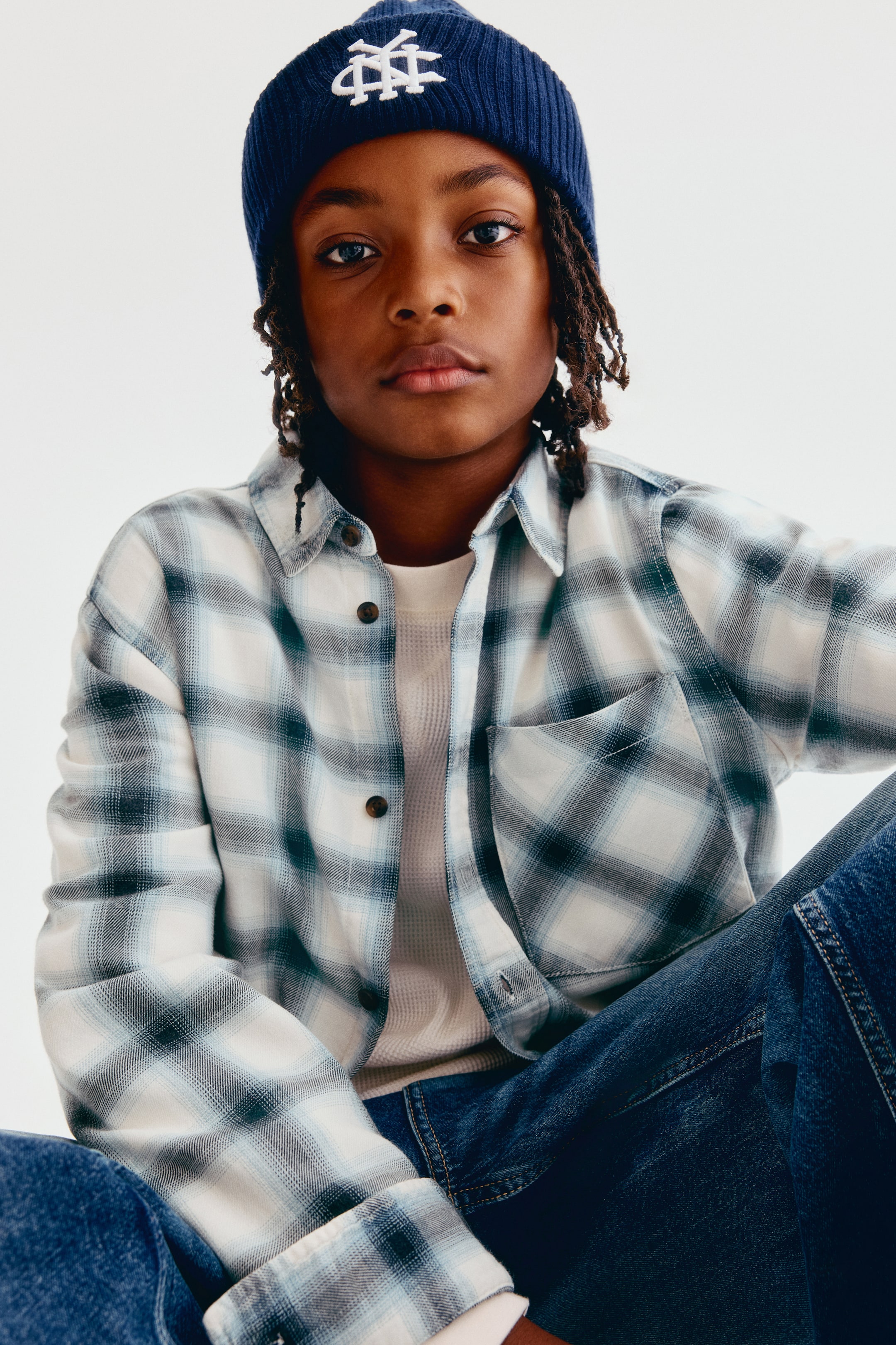 View larger image: A plaid cotton-weave shirt is shown from the front, featuring a turn-down collar, front button closures, and a single open chest pocket. The shirt is layered over a white waffle-knit T-shirt, with its long sleeves extending to the wrists.