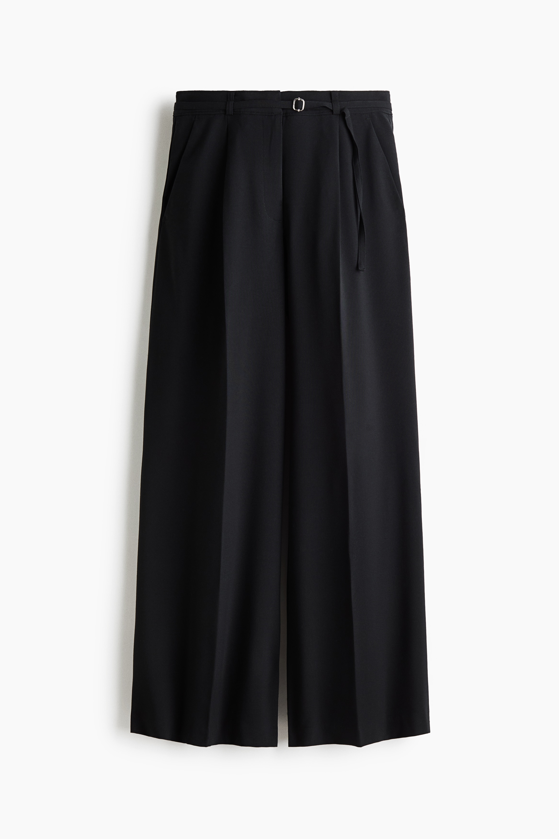 Wide-leg black tailored trousers featuring pressed creases down the front are worn by the model. The loose-fitting trousers are styled with a bright red long-sleeved button-up shirt and a grey knitted jumper tied around the waist.