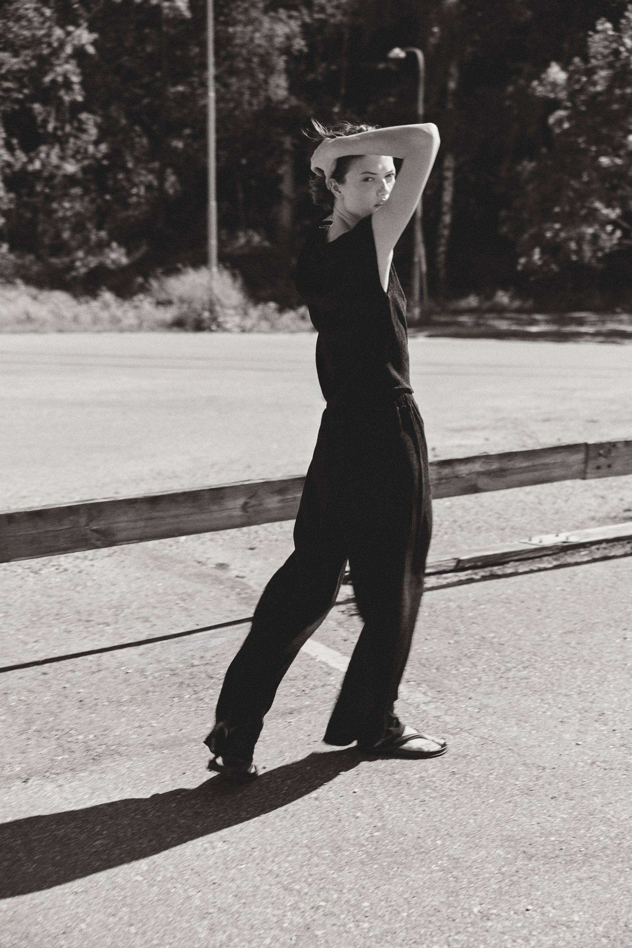 View larger image: The model is wearing relaxed-fit trousers made of crinkled jersey, showcasing a high, elasticated waist with a drawstring and straight legs. She has paired the trousers with a dark sleeveless top and flat sandals.