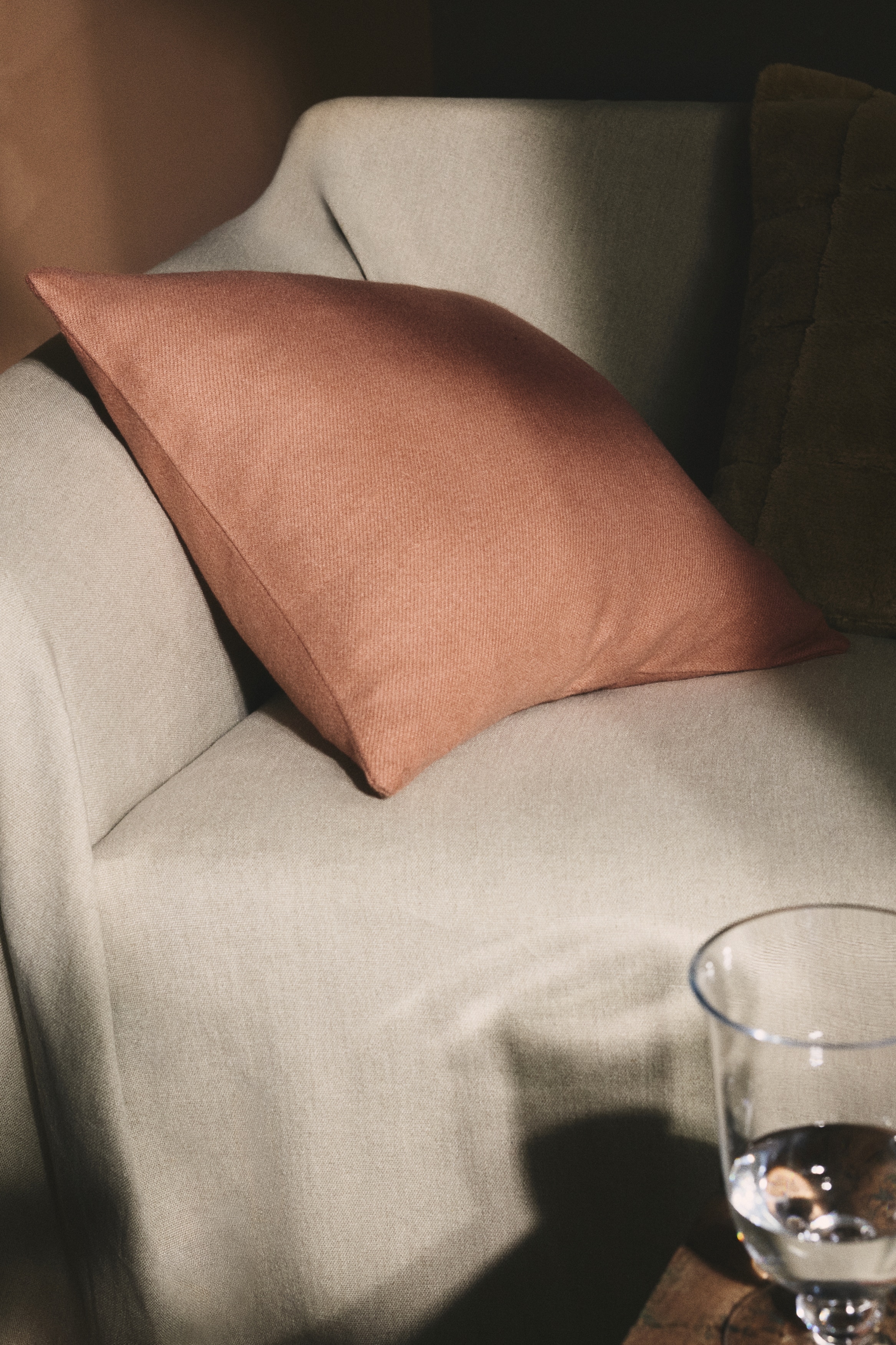 A cushion cover is presenting as front, featuring a muted peach felted viscose-blend weave. A zip is running along one side.