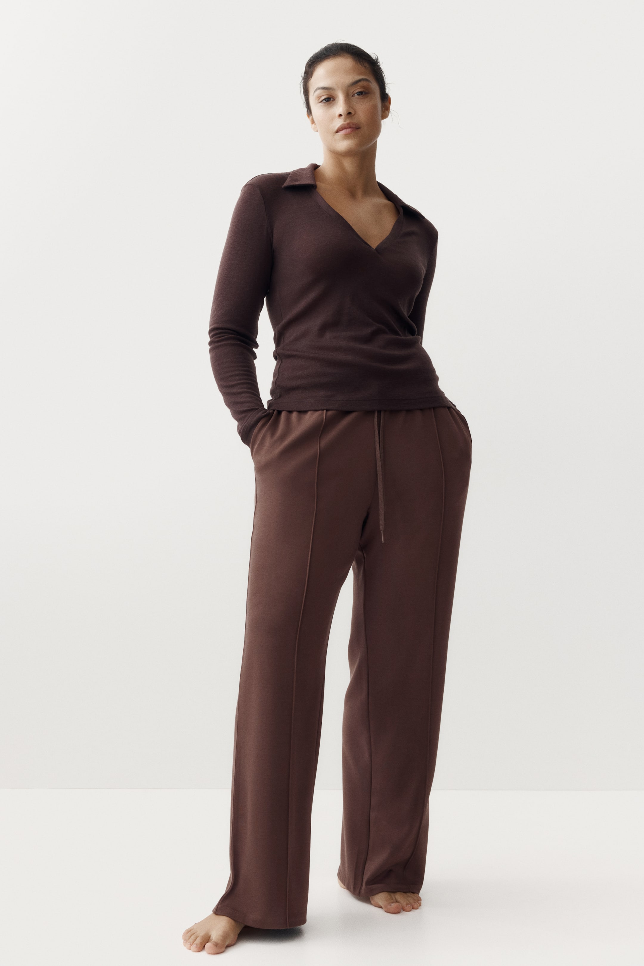 View larger image: A dark brown matching set is showcased, featuring a long-sleeve polo top with a V-neck and collar, and coordinating wide-leg pants with a drawstring waist and visible vertical front seams. The top is styled tucked into the pants.