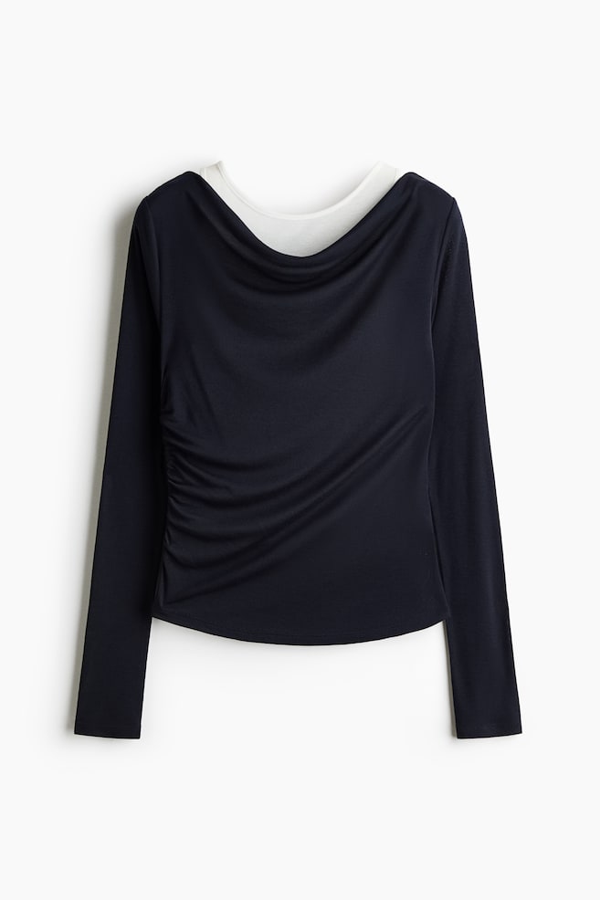 Se muestra de frente una blusa de manga larga en azul marino oscuro, con un escote tipo cowl drapeado que deja ver una capa interior blanca. La blusa estÃ¡ diseÃ±ada con fruncido lateral en un costado, creando un suave drapeado diagonal sobre el cuerpo. - 1