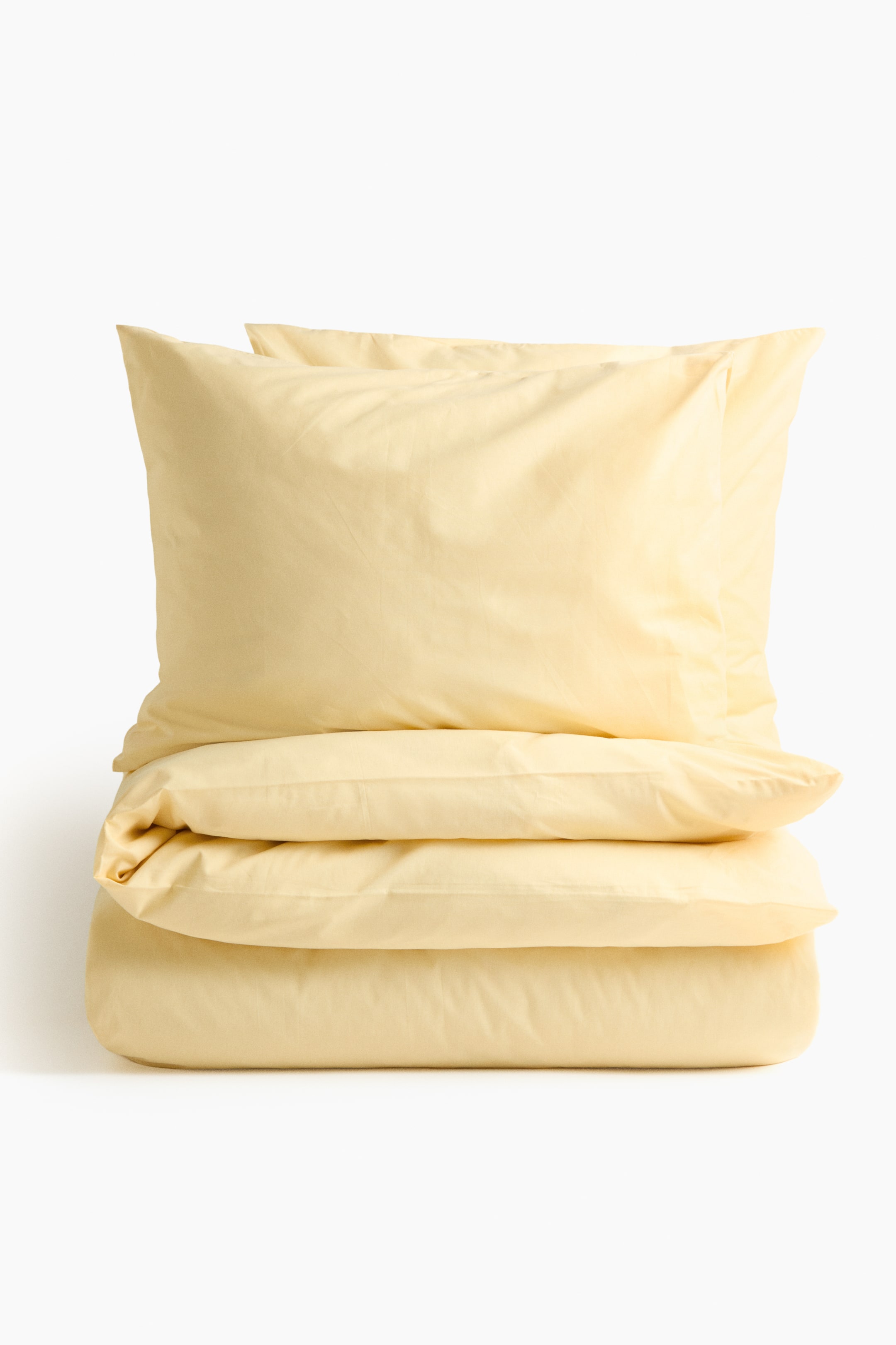 Ver imagen más grande: Un conjunto de funda de edredón amarillo claro se presenta como una pila ordenada, con una funda de edredón doblada en la base y dos fundas de almohada esponjosas descansando encima.