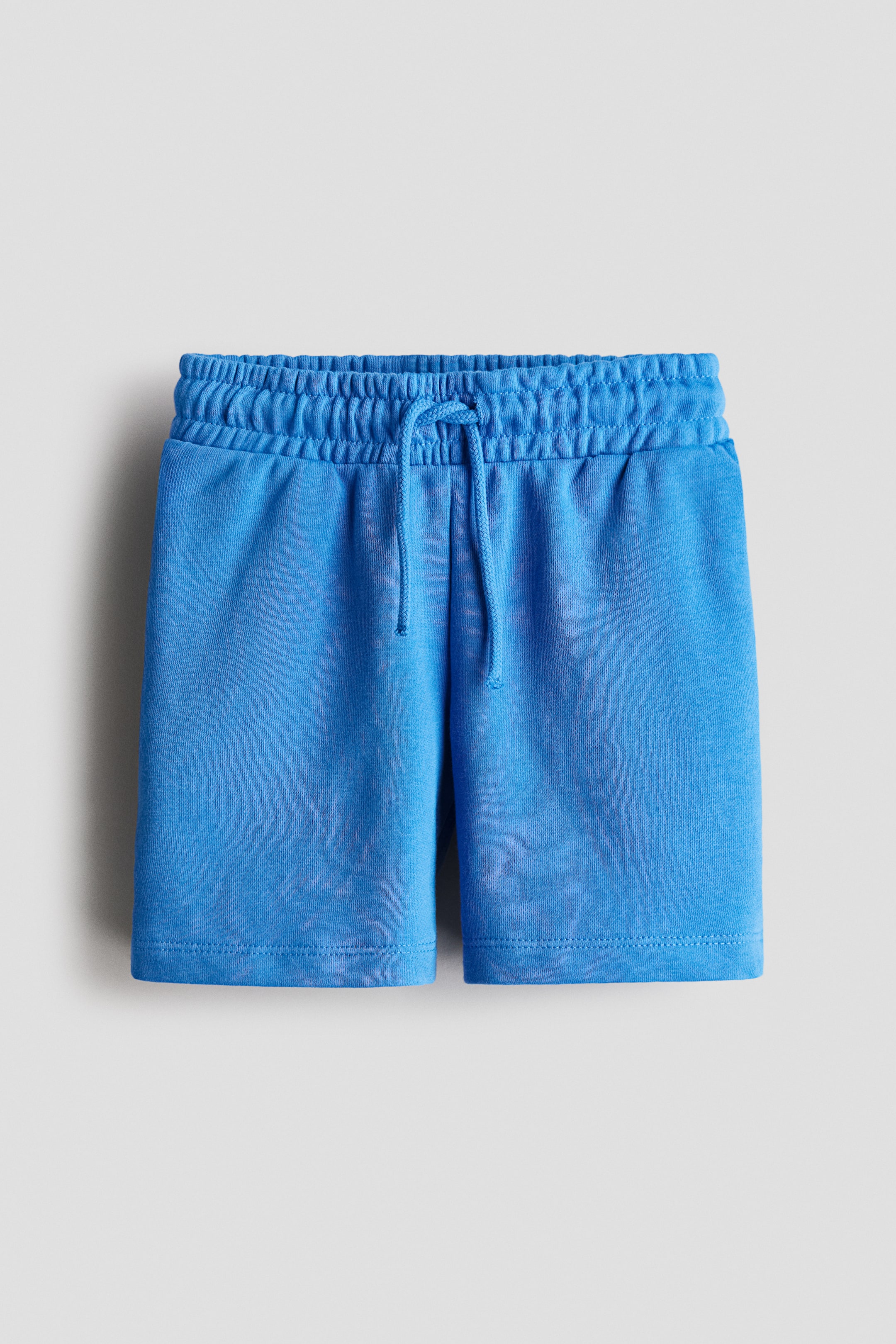 View larger image: Blue knit shorts are displaying an elasticated waistband with a matching drawstring tied at the front, and plain stitched hems.