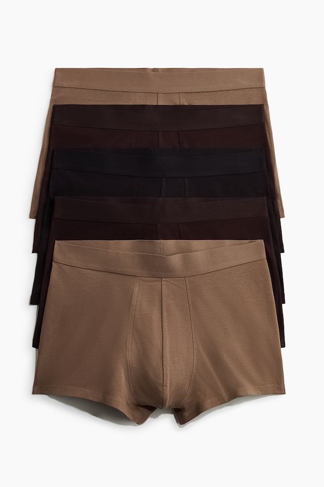 Five pairs of men's boxer briefs are stacked, displaying varying shades of brown and black. Each brief is featuring an elastic waistband and prominent front panel stitching. - 1