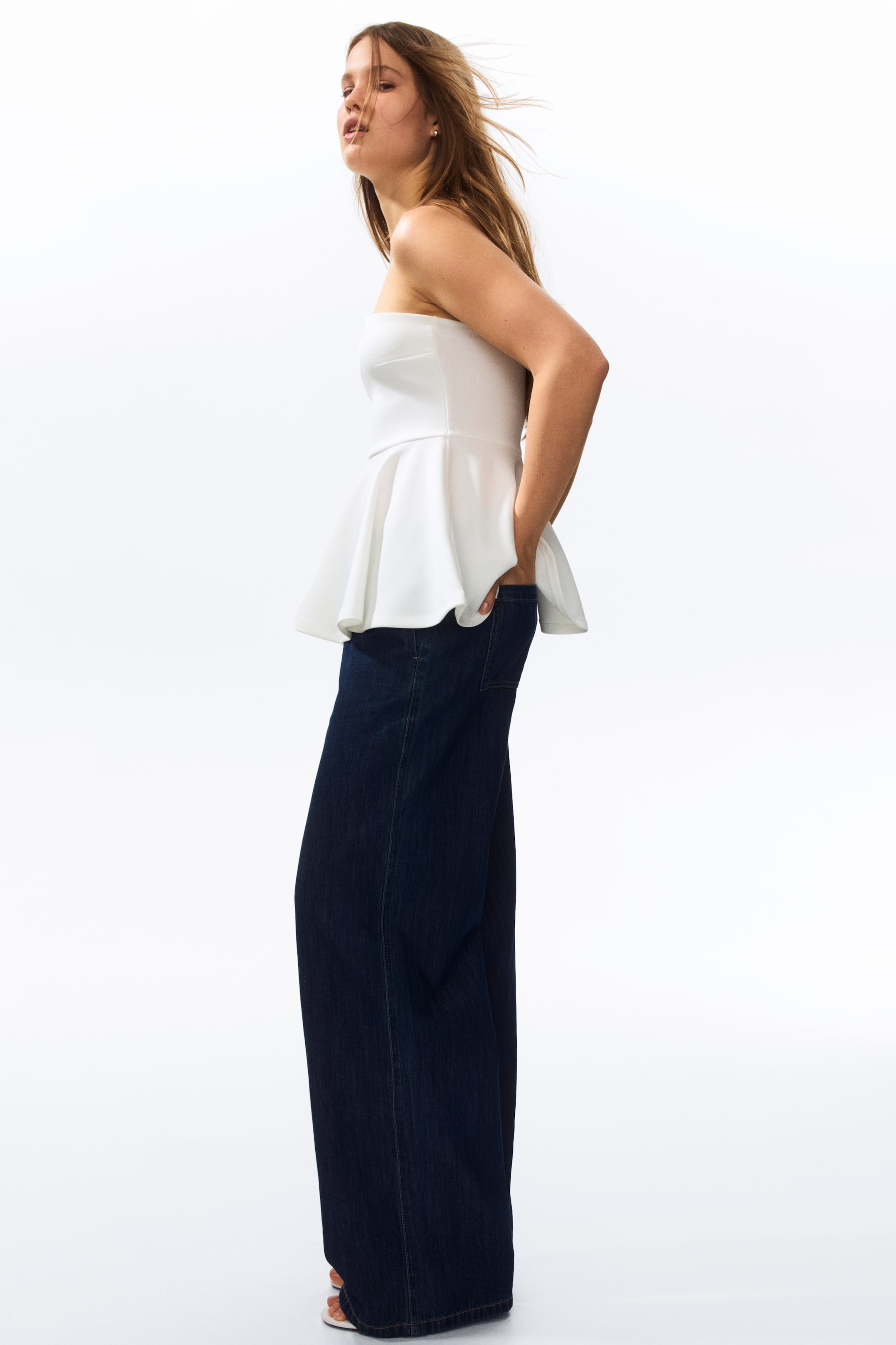 Büyük resmi görüntüle: Modelin bir elini yan cebine koyarak poz verdiği koyu yıkama, geniş paça denim pantolon.