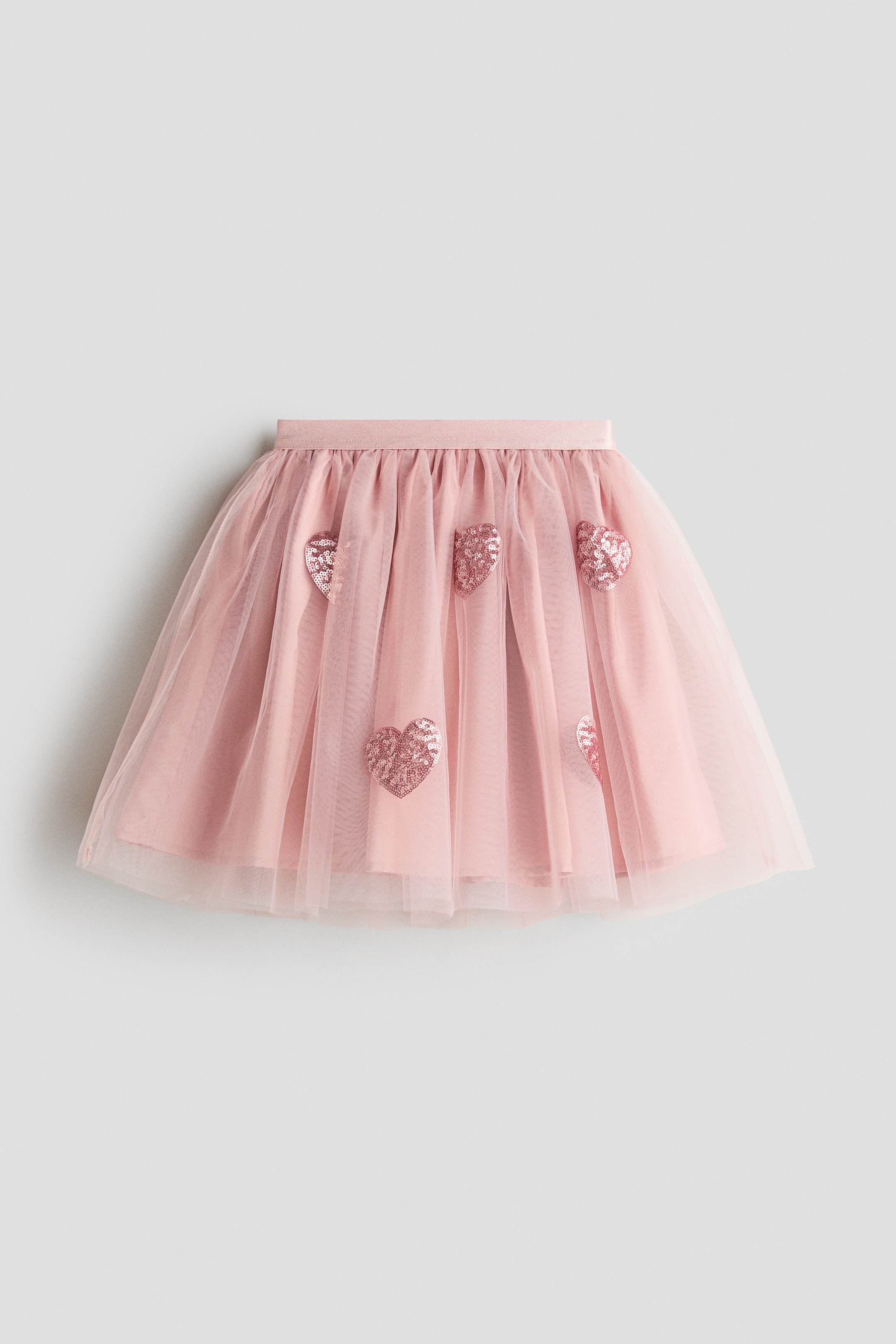 Voir une image plus grande: Une jupe évasée en tulle rose est présentée de face, avec une taille élastiquée froncée qui crée du volume. La couche extérieure en tulle transparent arbore des motifs de cœurs à paillettes roses dispersés sur une doublure rose unie.