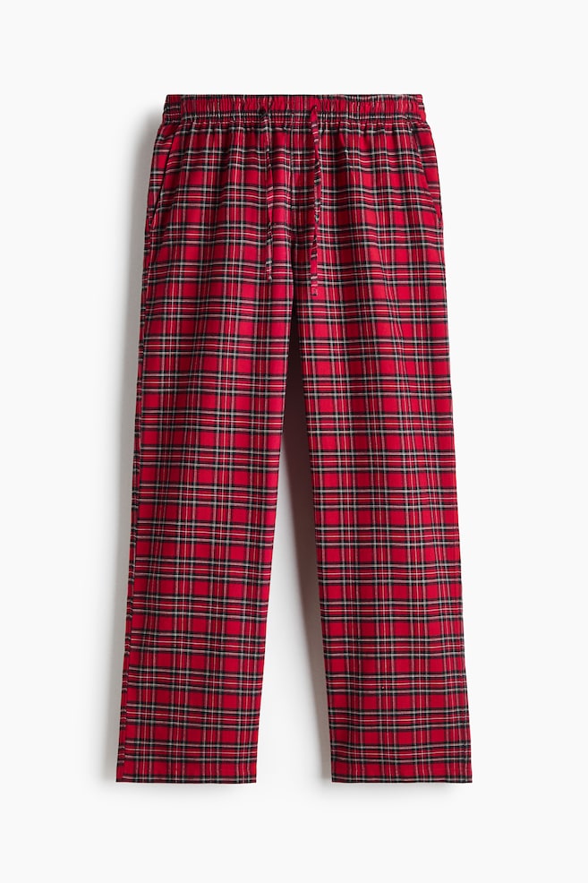 Pants in red and black plaid cotton flannel are hanging front-facing, showcasing a relaxed fit with straight legs. They feature an elasticated drawstring waist, a mock fly, and diagonal side pockets. - 1