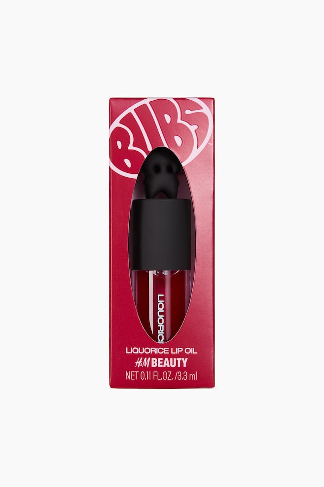 The product is a red rectangular box, facing front, featuring a central oval cutout that is revealing a clear bottle containing red liquid. The bottle is displaying "LIQUORICE" vertically on its side and is topped with a uniquely shaped black cap, while the box is also displaying "BIBS", "LIQUORICE LIP OIL", and "H&M BEAUTY" text. - 1