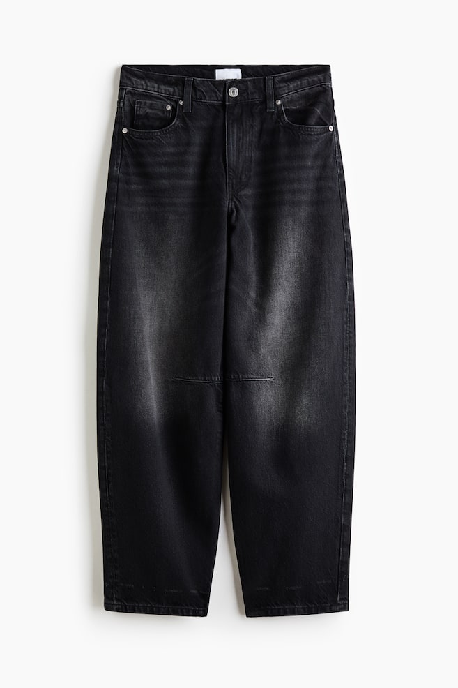 A pair of faded black denim jeans is shown facing front, showcasing a regular waist and a curved, voluminous leg silhouette that tapers toward the hems. The design is featuring a classic five-pocket layout, a button closure, and horizontal dart seams across the knees. - 1