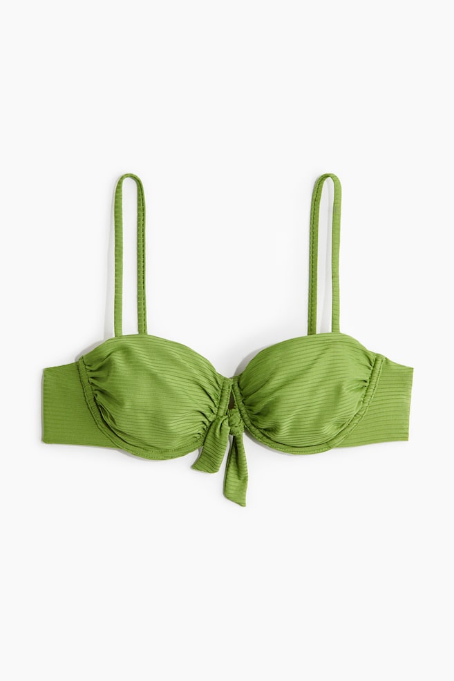 A green bikini top is lying flat, front-facing, featuring a ribbed texture throughout. It is designed with underwire cups, thin shoulder straps, and a tied knot detail at the front center. - 1