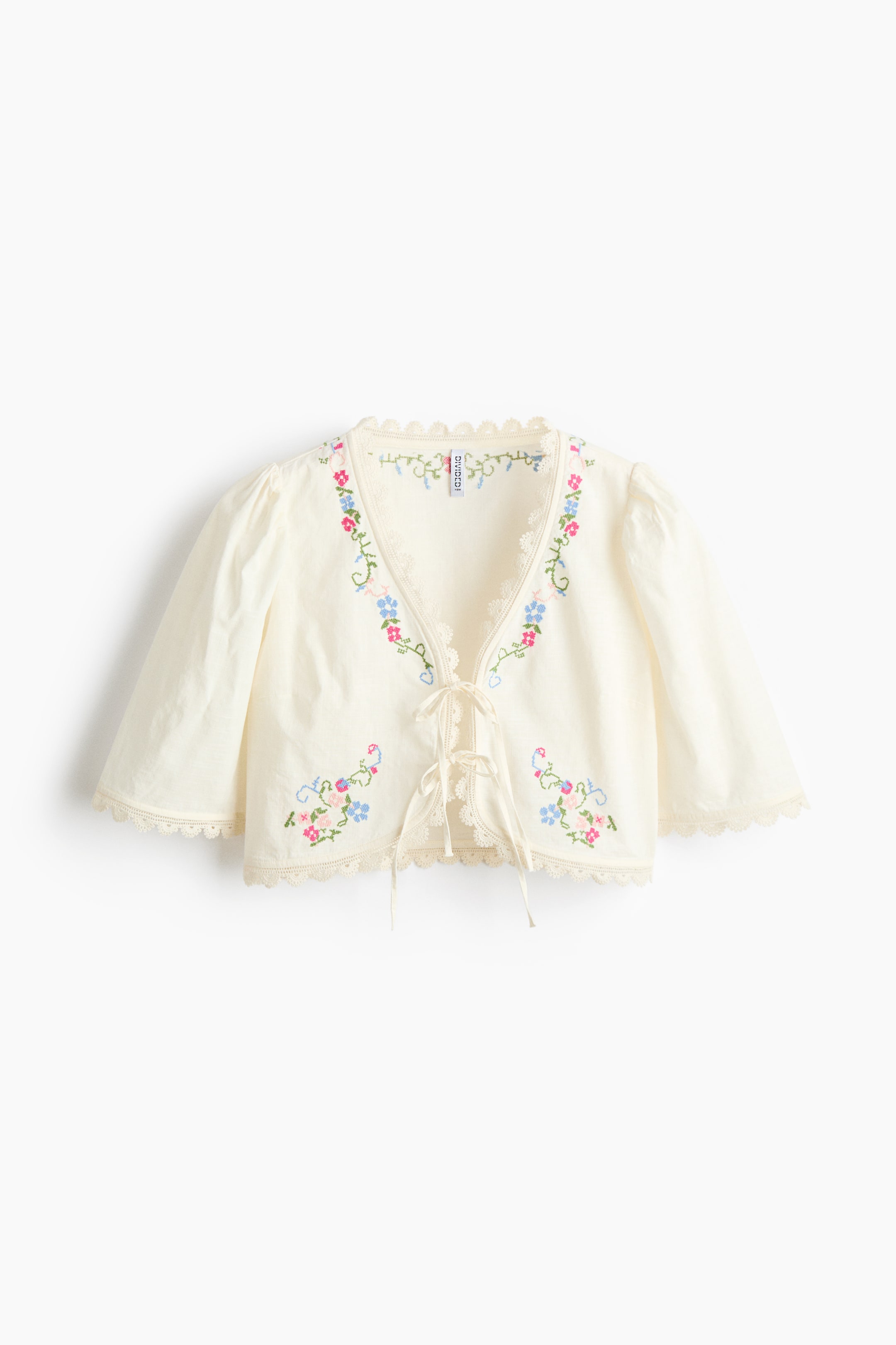 View larger image: A cream cropped cardigan is showcased FRONT, featuring elbow-length puffed sleeves and a tie-front closure. It is embellished with vibrant floral embroidery and scalloped lace trim along the V-neck, front opening, hem, and sleeve cuffs.