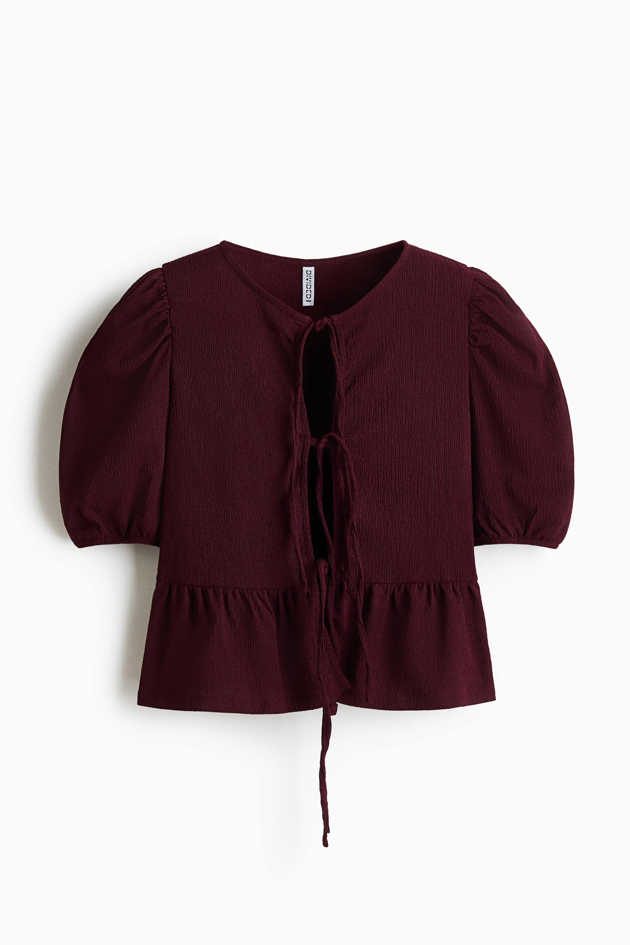 拡大画像を表示: 正面から見たマルーンのペプラムトップ。しわ加工のテクスチャーが特徴で、ショートのパフスリーブと、垂れた紐で留める開いたネックラインのデザインです。